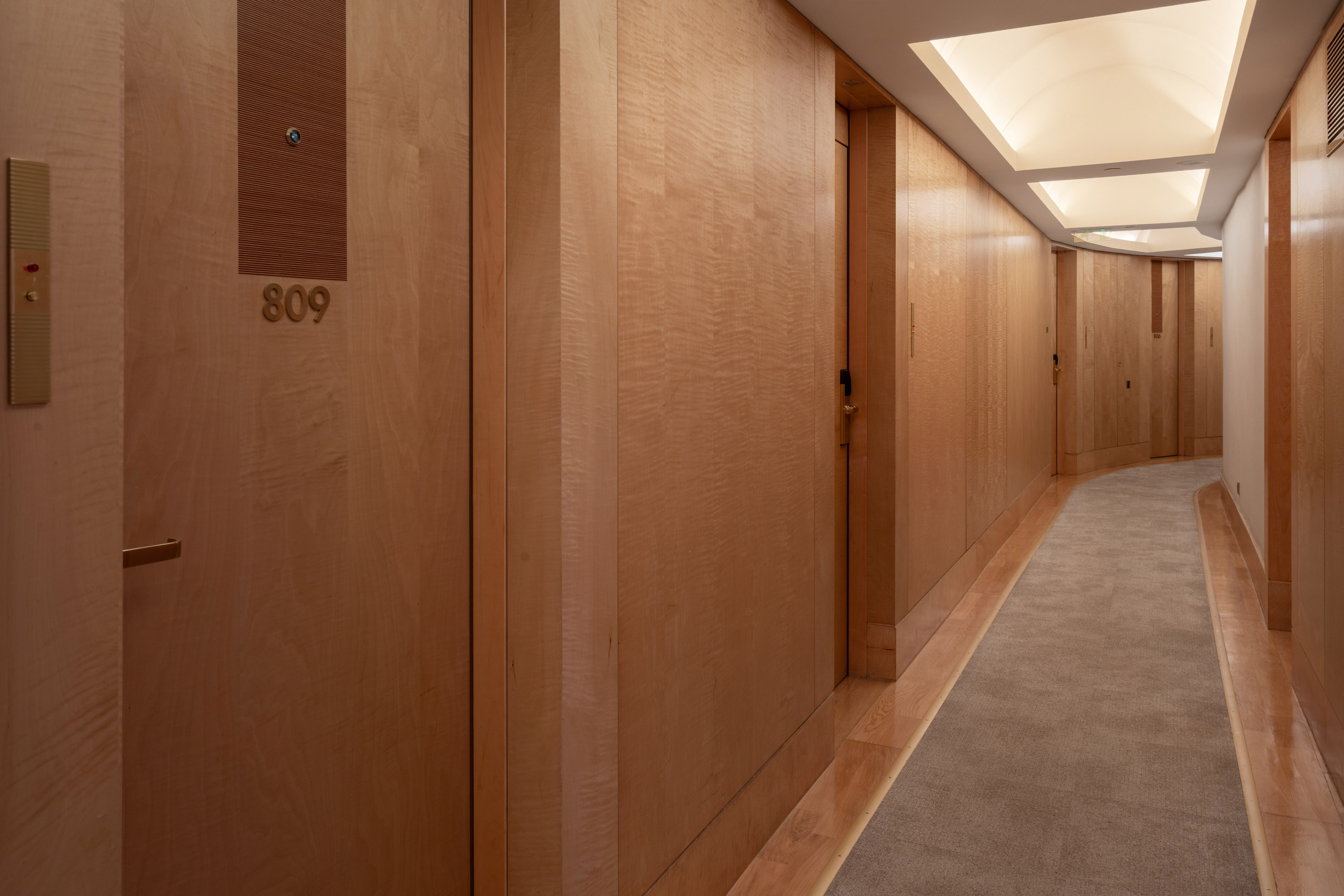 Modern hotel hallway with light wood paneling, illuminated ceiling, and room 809.