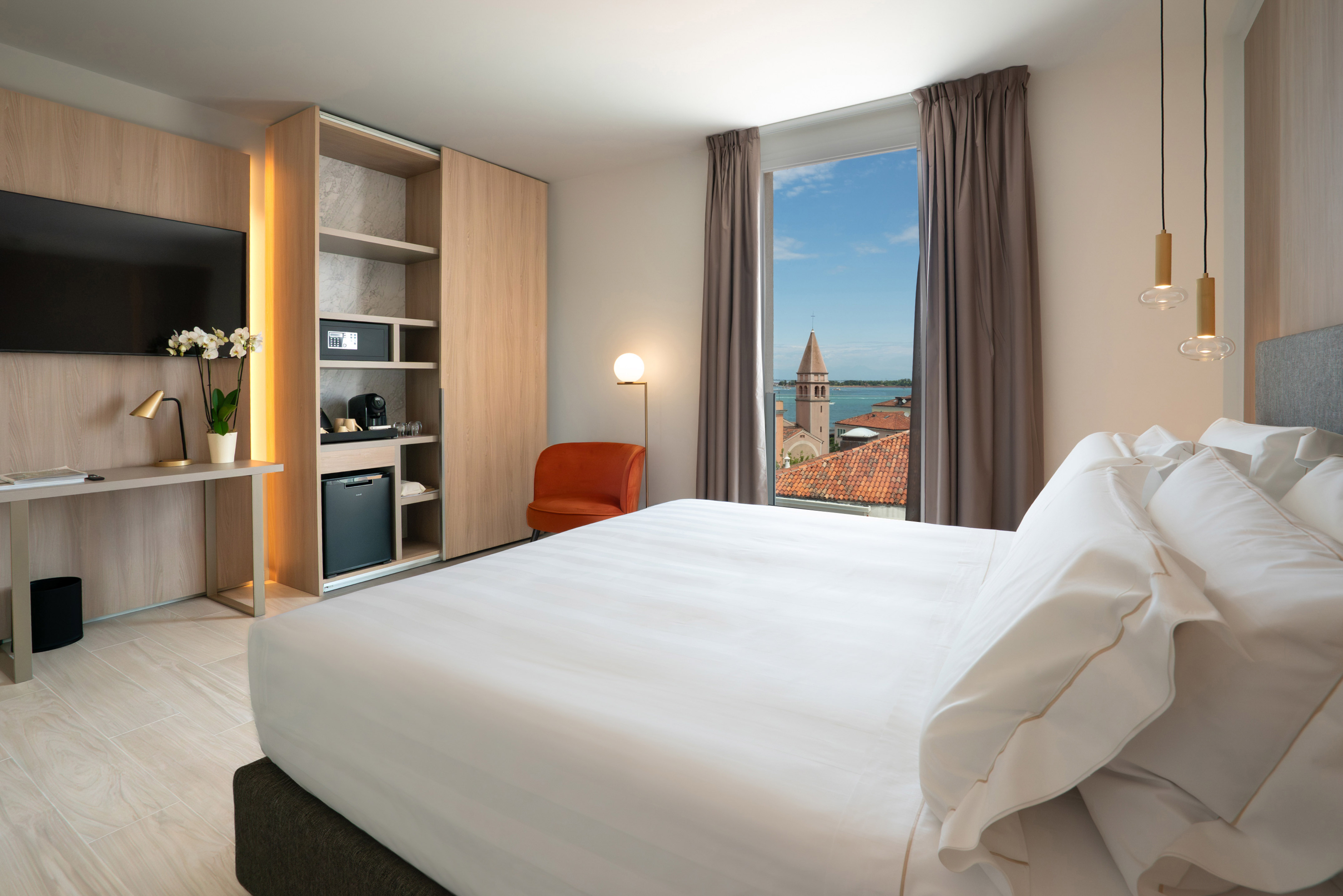 Modern hotel bedroom with large bed and sea view of historic bell tower.