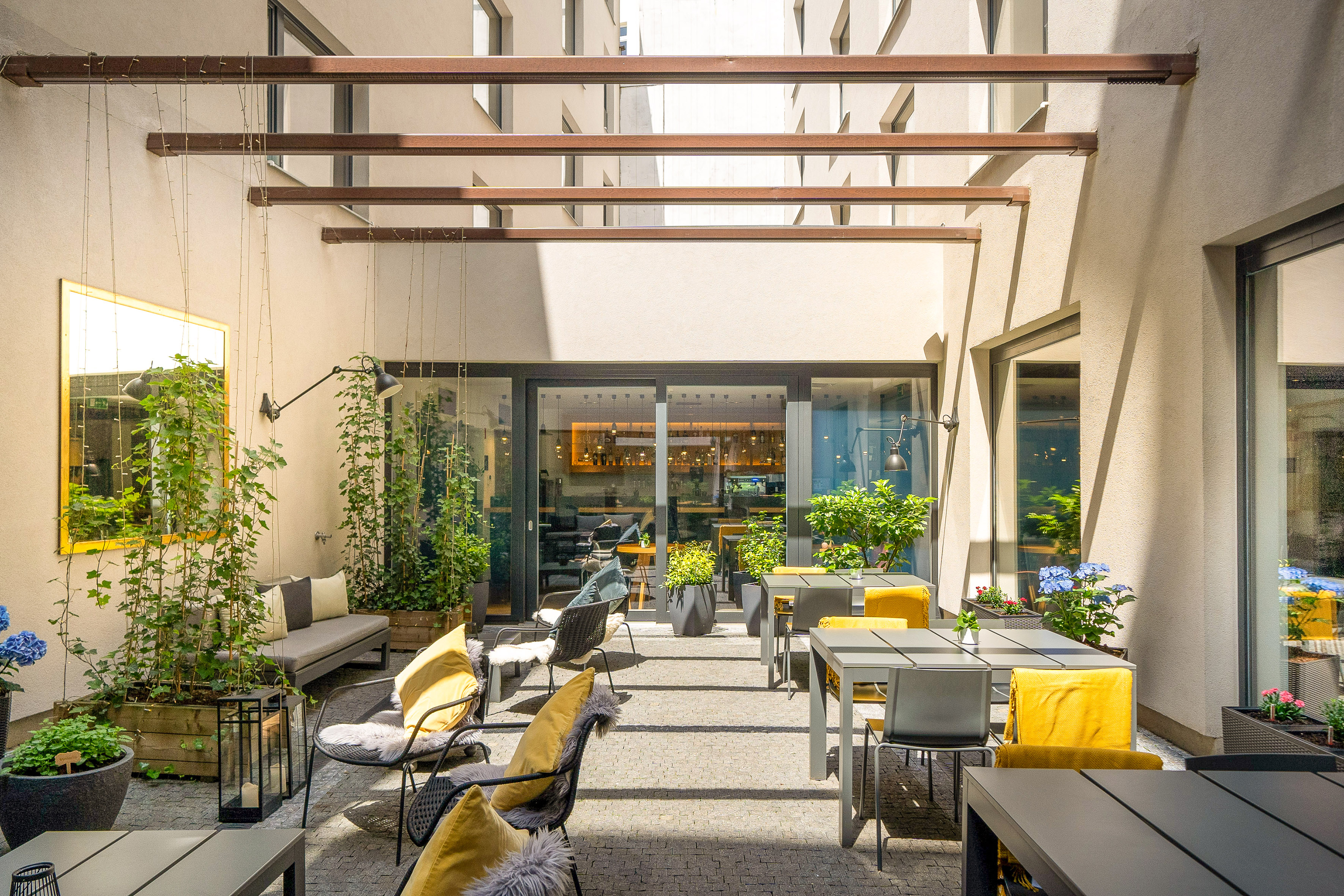 Modern hotel patio with outdoor seating, yellow cushions, and lush greenery.