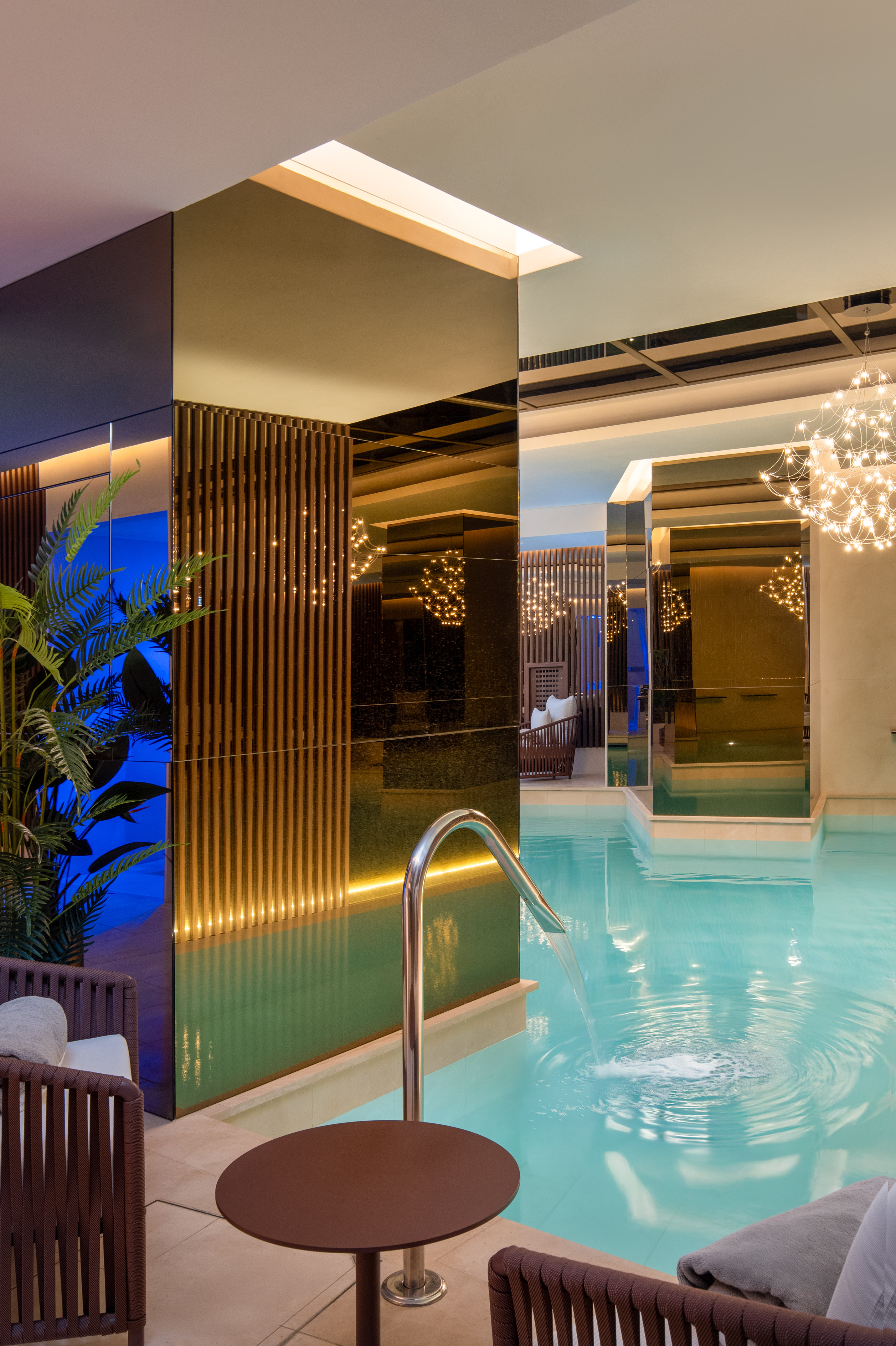 Modern indoor spa pool with water feature, mirrored decor, and ambient lighting.