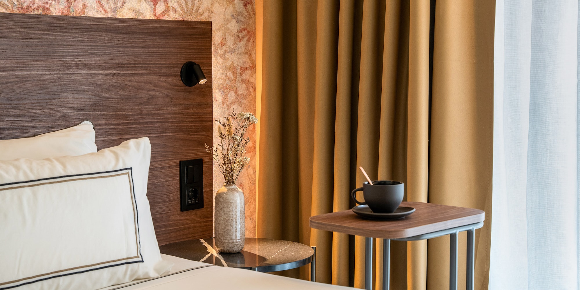 a bed with a cup of coffee and a table in front of a curtain