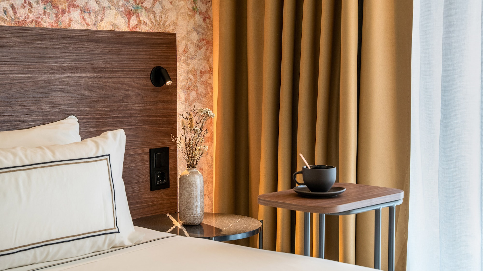 a bed with a cup of coffee and a table in front of a curtain