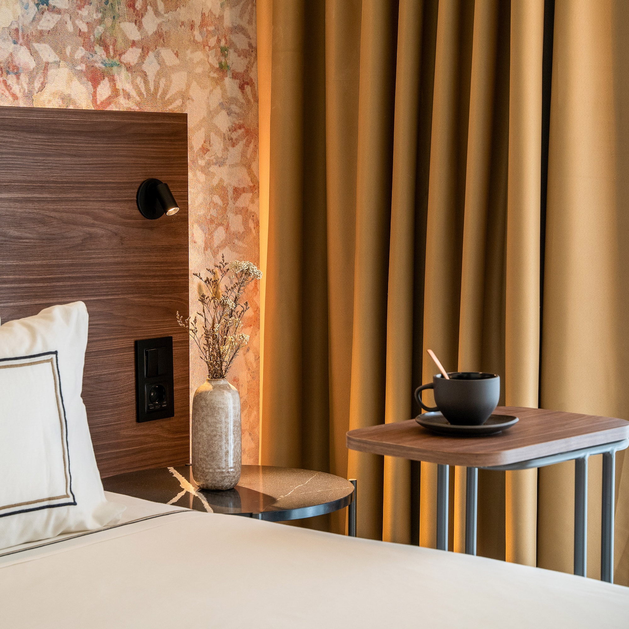 a bed with a cup of coffee and a table in front of a curtain