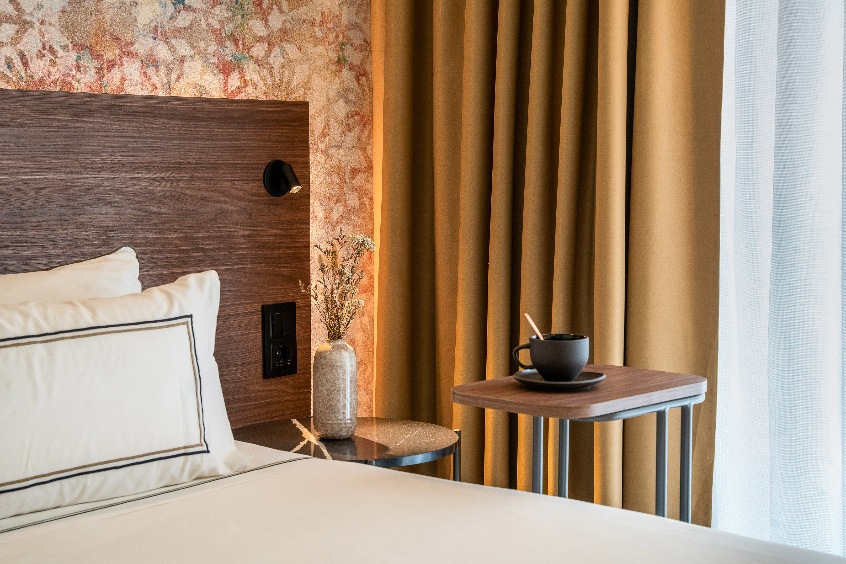 Stylish hotel room with bed, wooden headboard, coffee cup, and golden curtains.