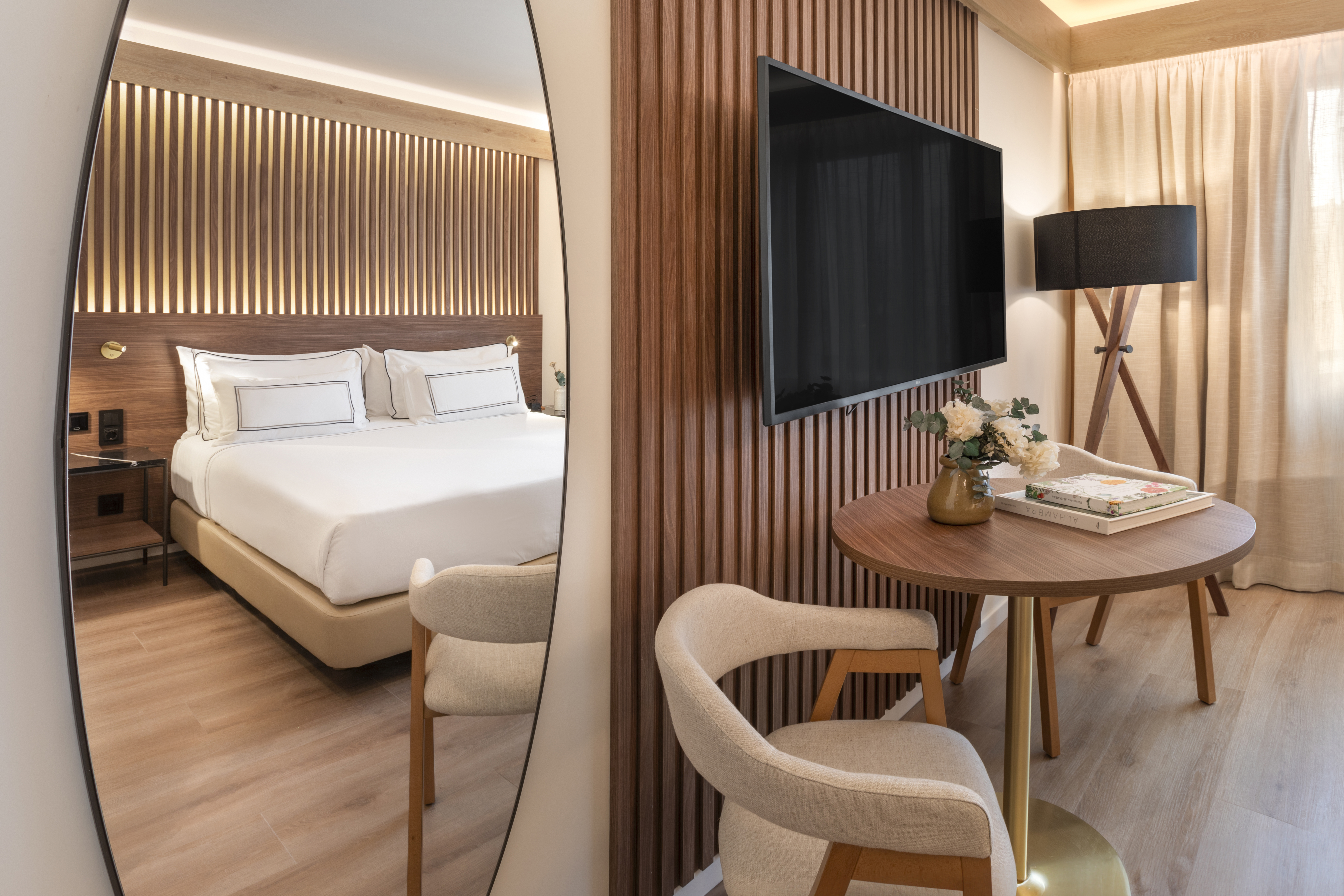 Modern hotel guest room with a cozy bed, wood walls, TV, and dining nook.