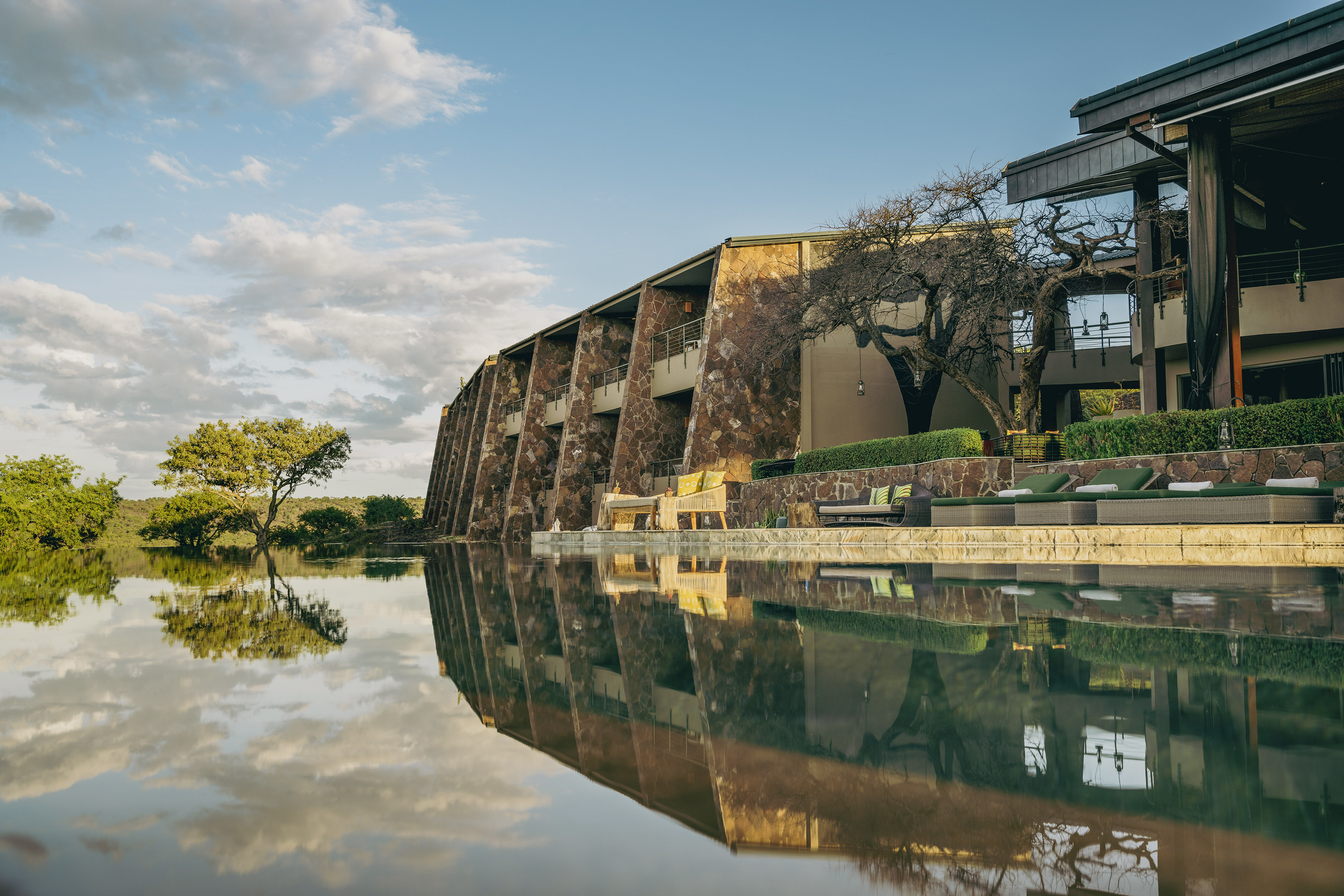 African safari lodge with infinity pool, stone architecture, and serene reflections.