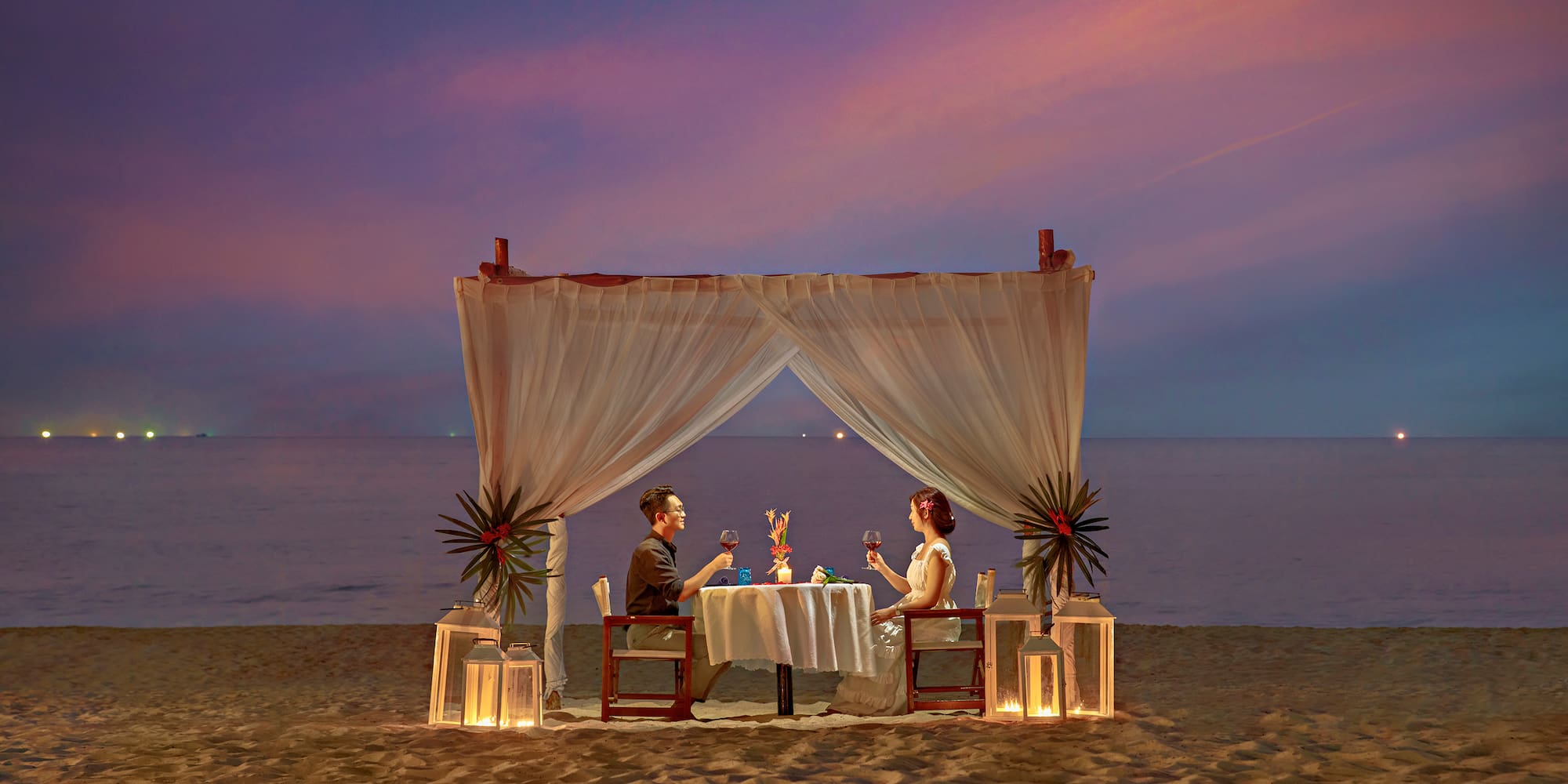 a man and woman sitting at a table on a beach