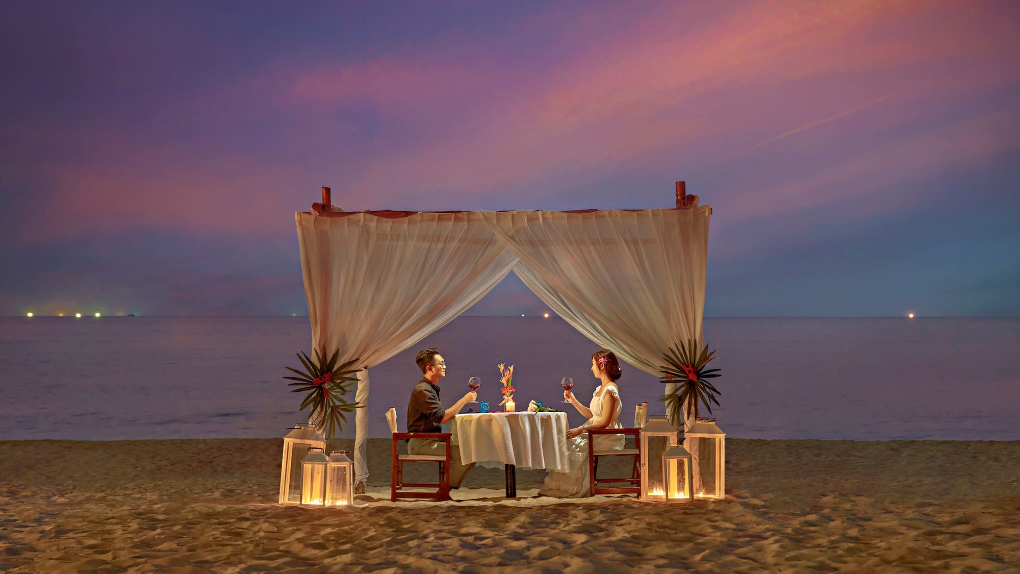 a man and woman sitting at a table on a beach