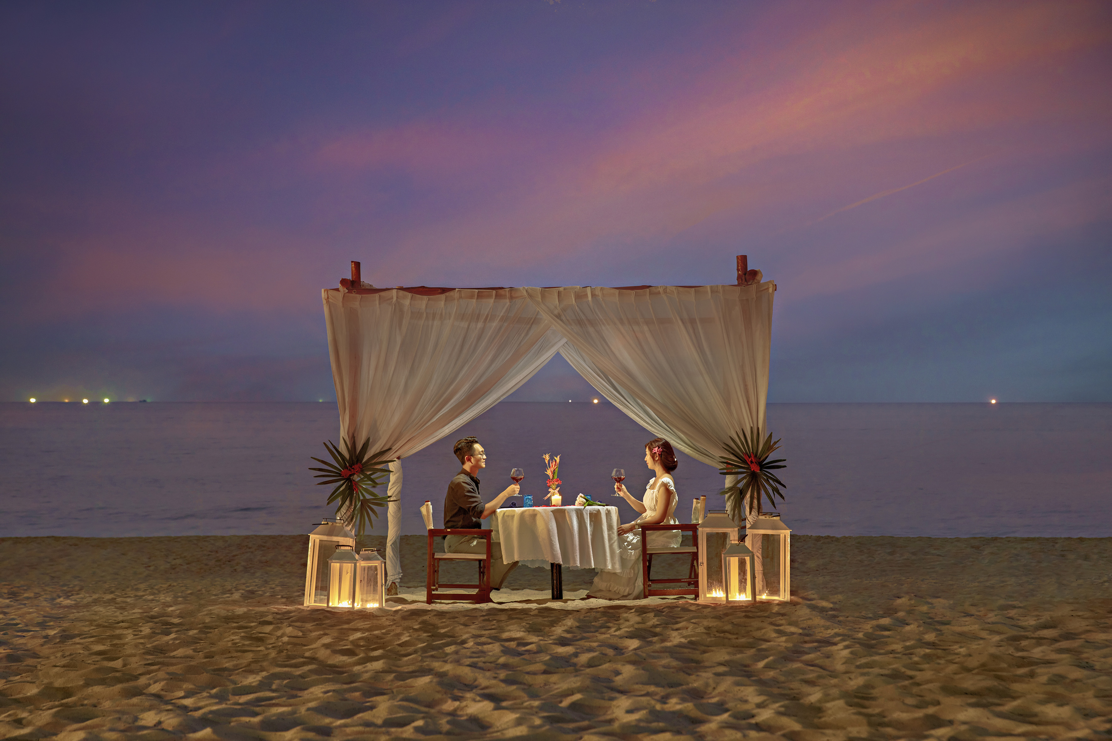 Romantic couple dinner on beach at sunset under canopy by ocean.