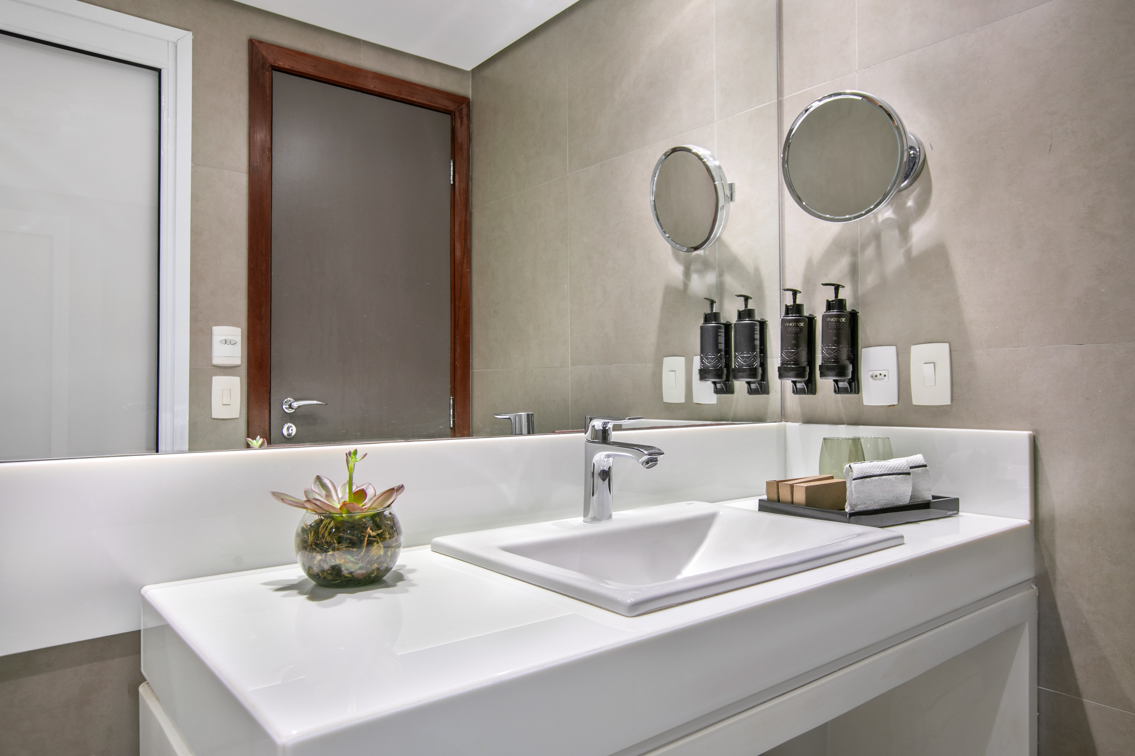 Sleek hotel bathroom with white vanity, sink, modern faucet, and amenities.