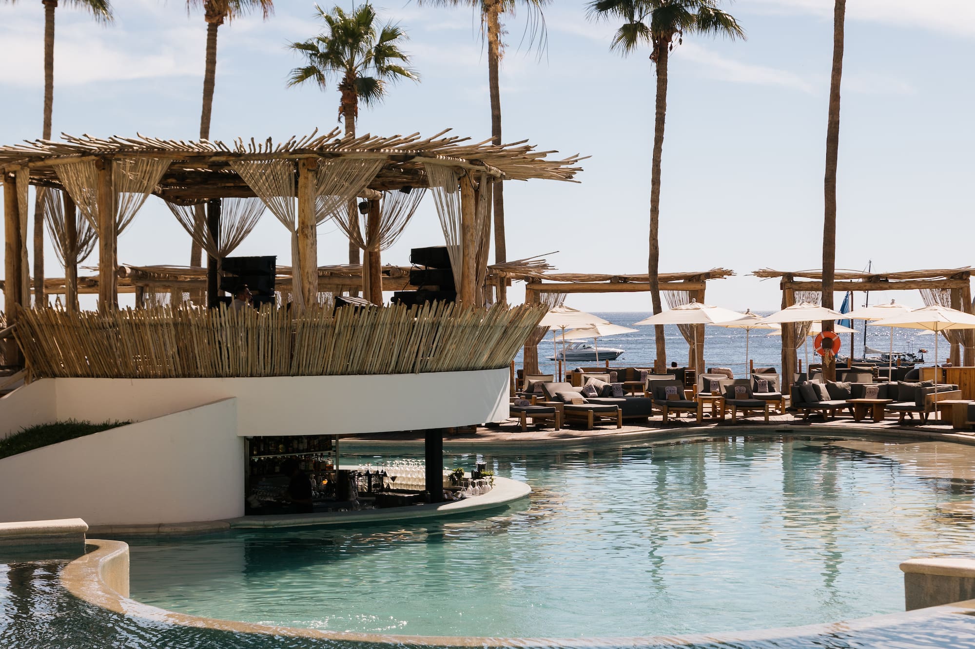 a pool with a bar and chairs and a deck with a large deck and palm trees