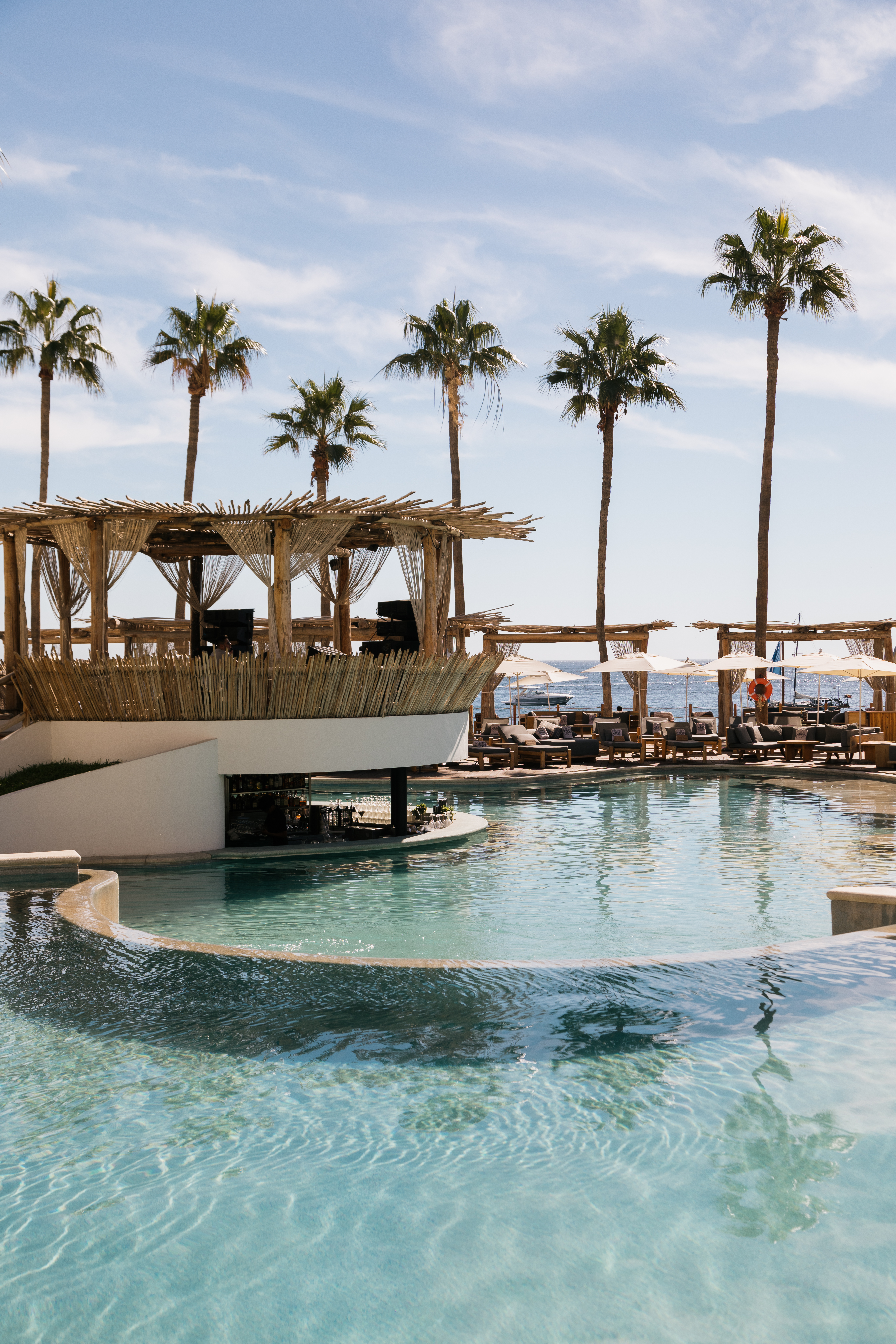 a pool with a bar and chairs and a deck with a large deck and palm trees
