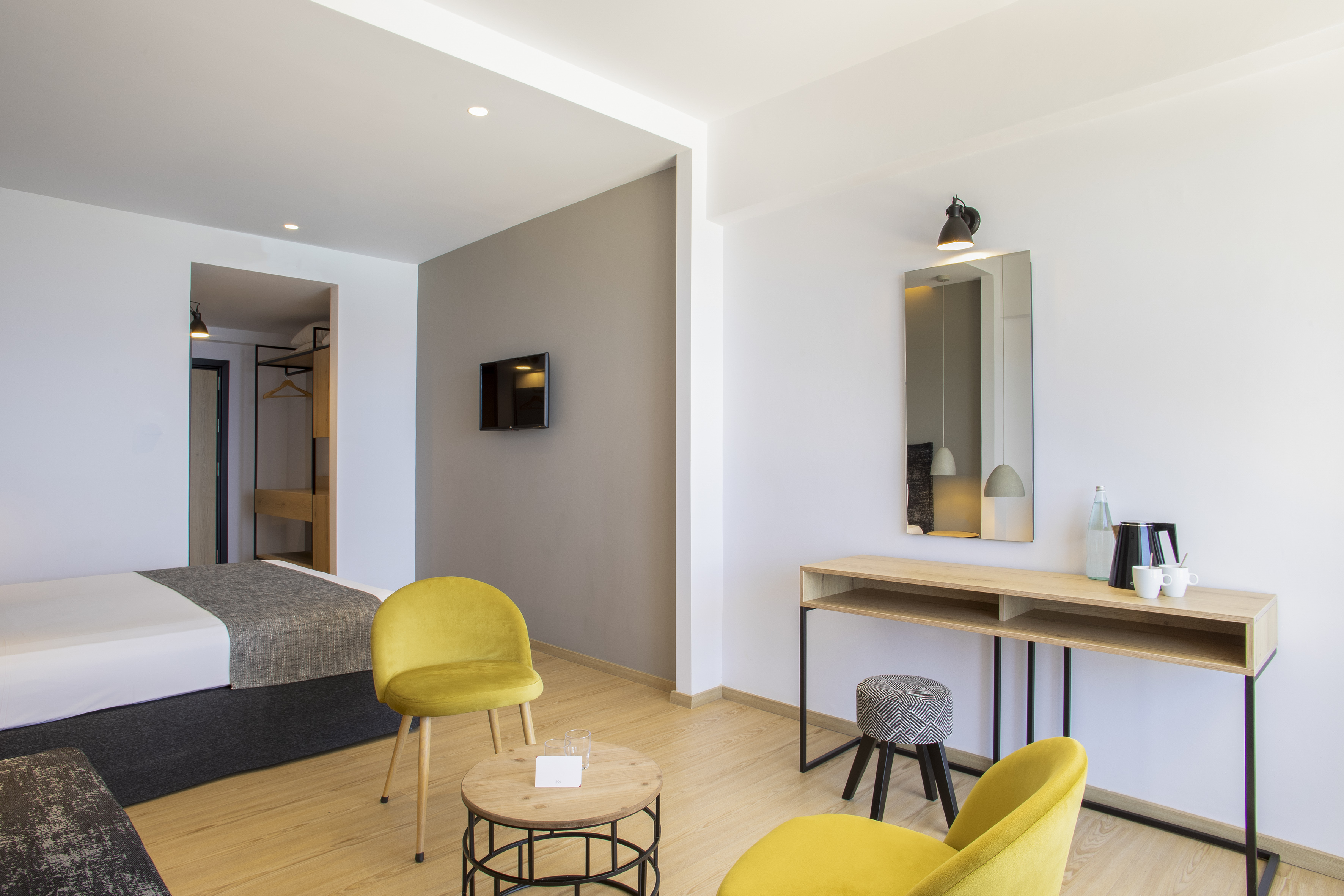 Modern hotel room with yellow chairs, wooden floor, bed, and console table.