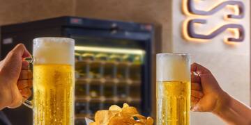 a person holding glasses of beer and a basket of chips