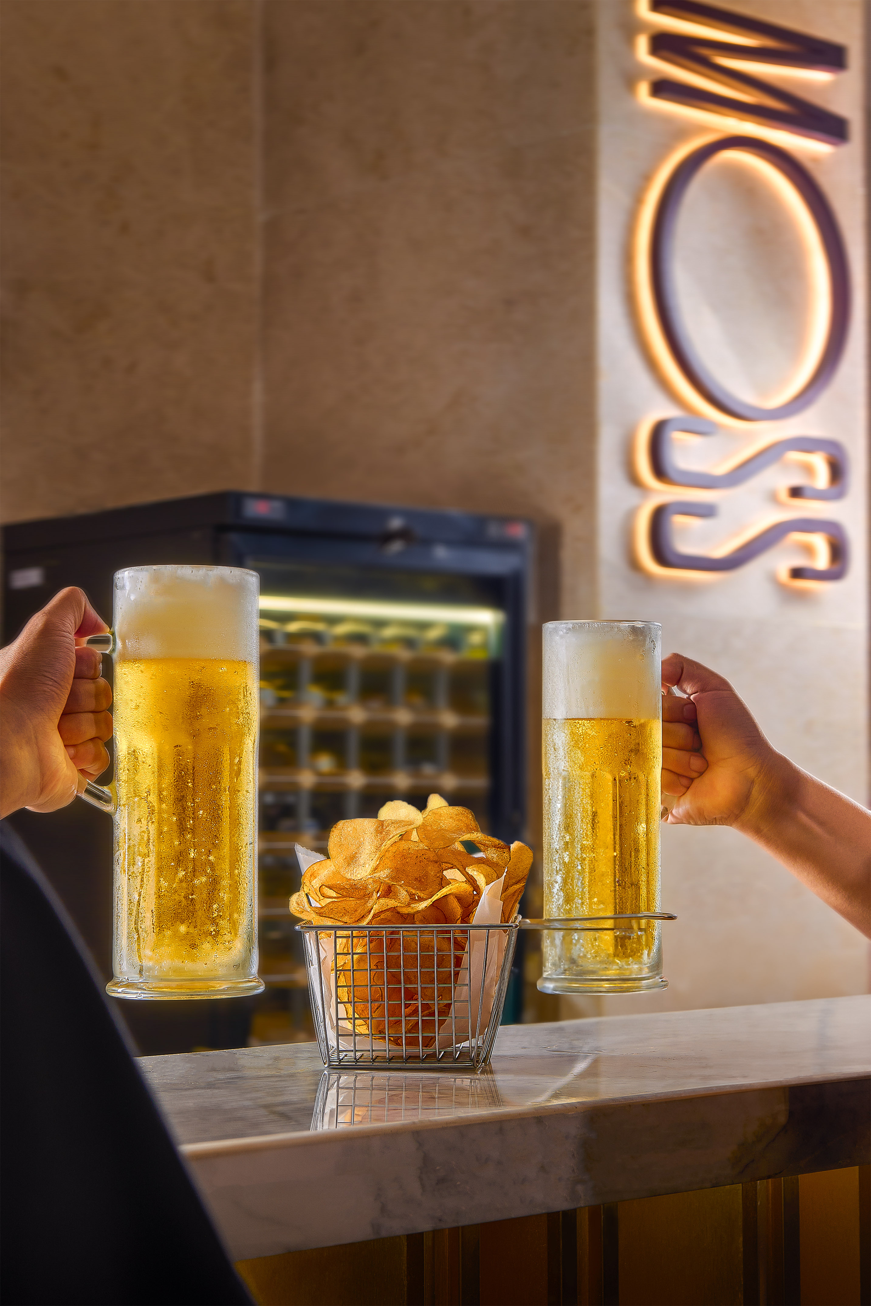 a person holding glasses of beer and a basket of chips