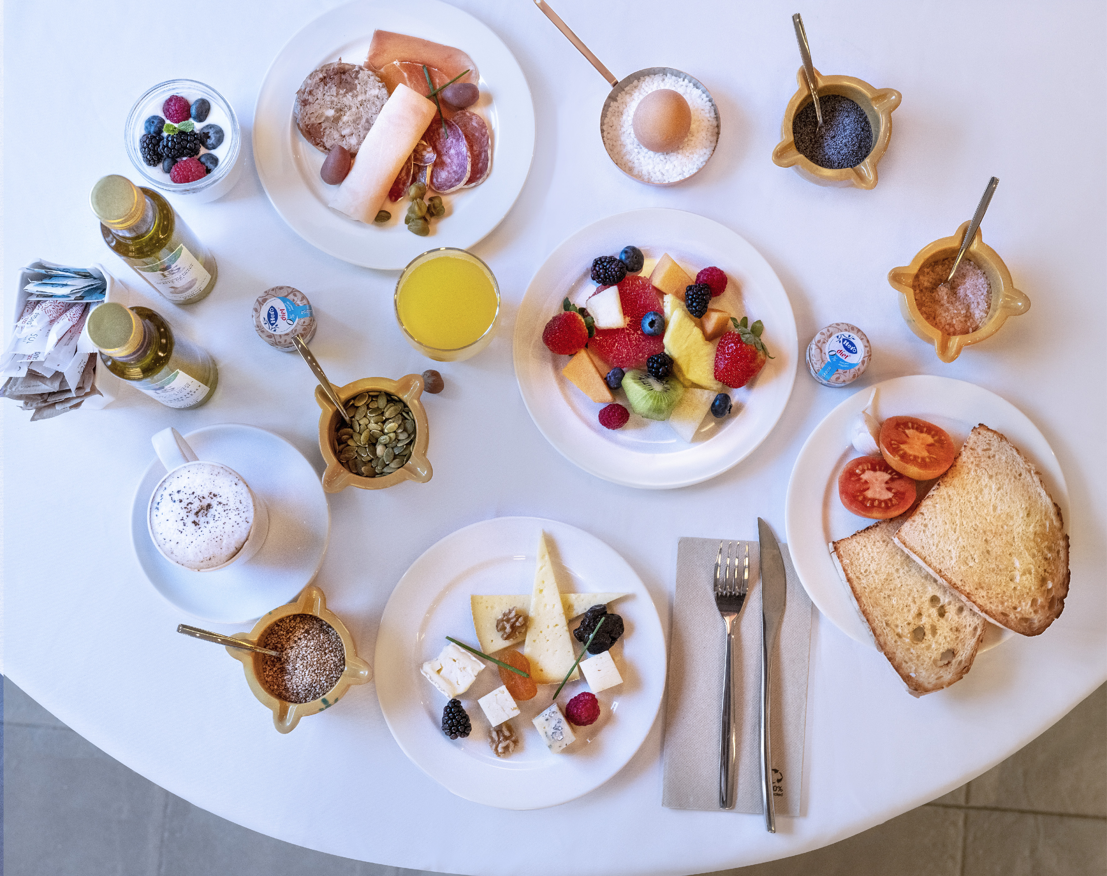 Diverse breakfast spread: fresh fruit, cold cuts, cheeses, yogurt, coffee, toast.