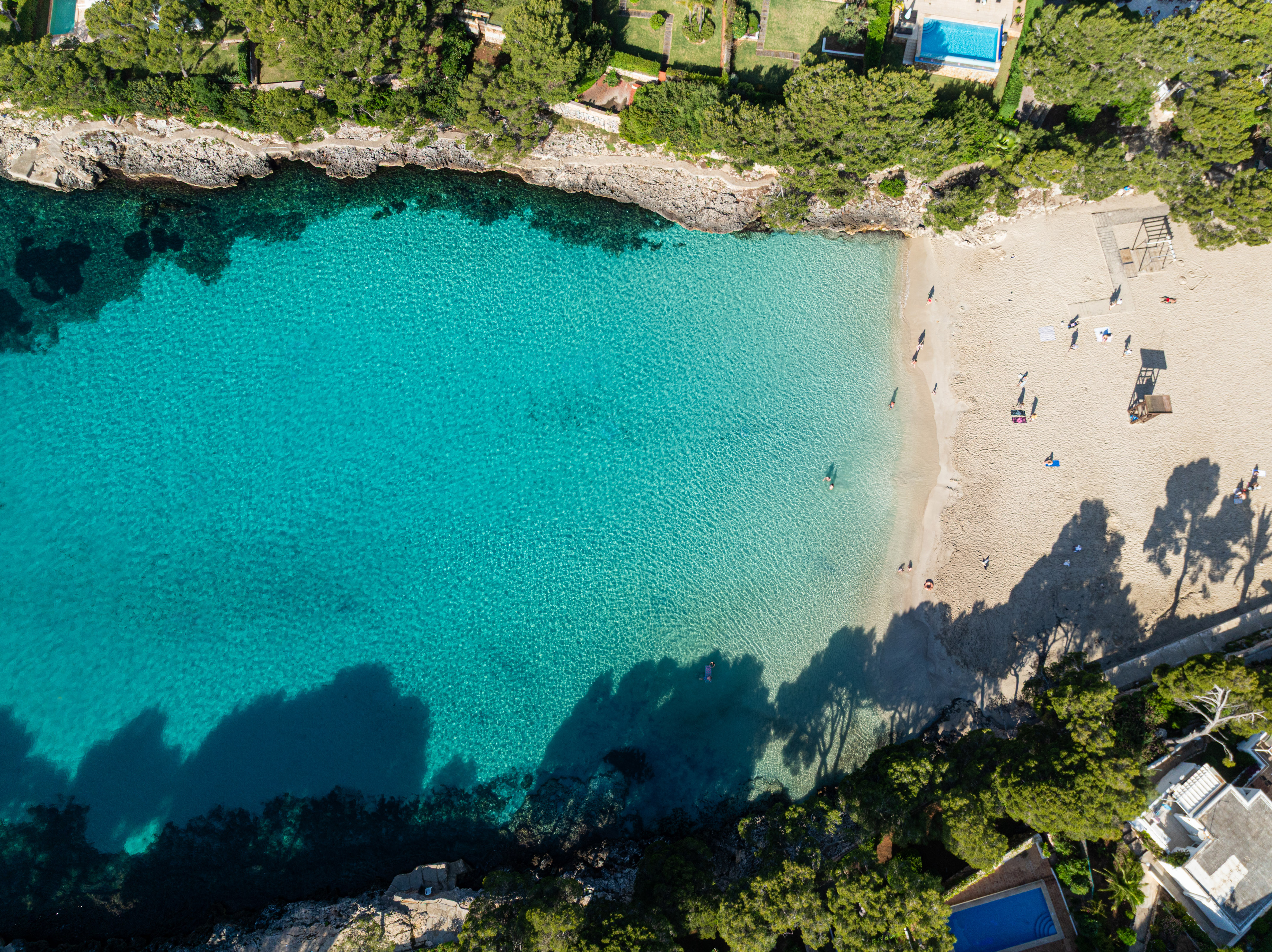Cala con playa de arena, agua turquesa cristalina y vegetación, vista aérea.