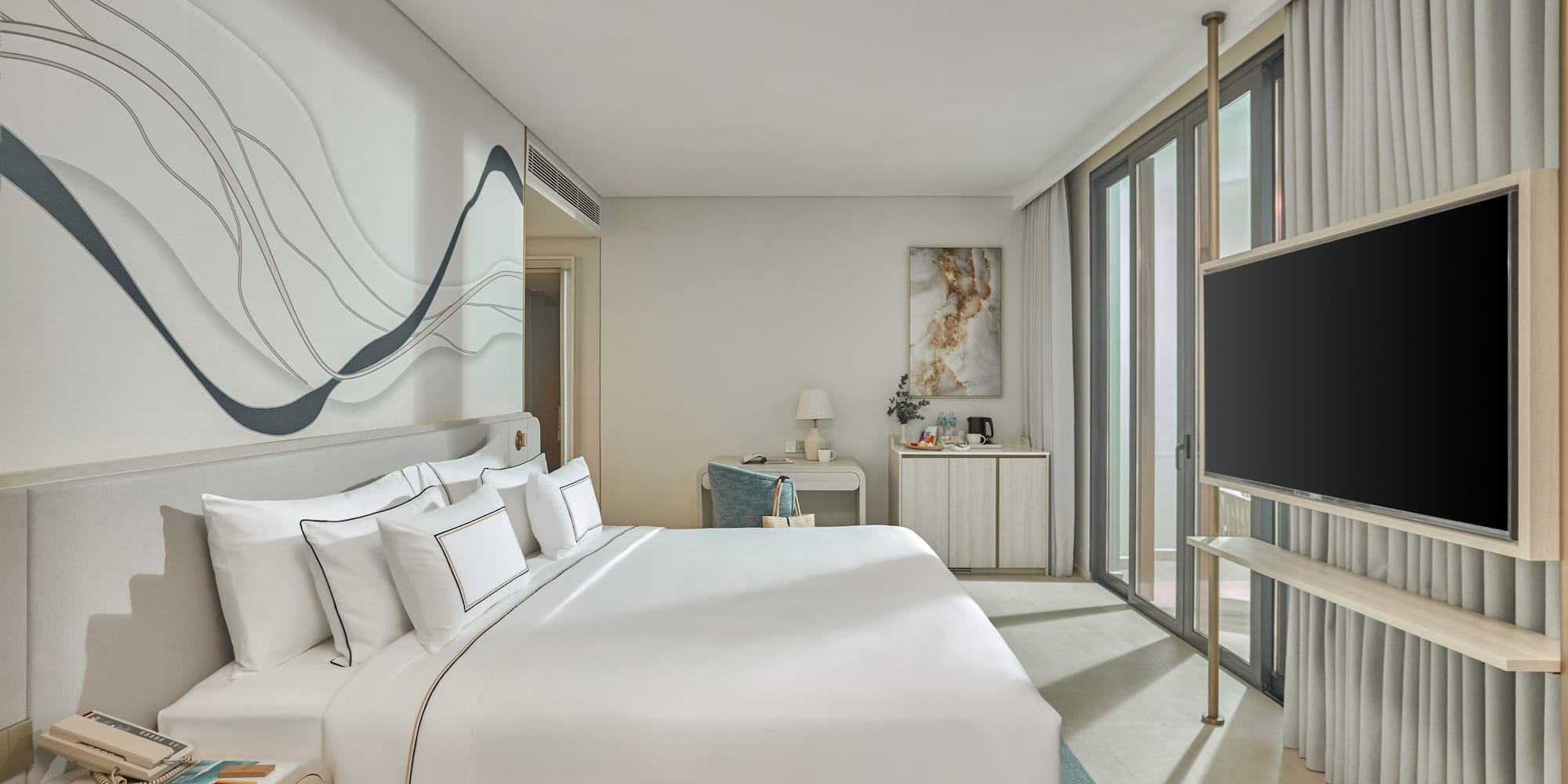 Modern hotel bedroom with white bed, abstract wall art, desk, and TV.