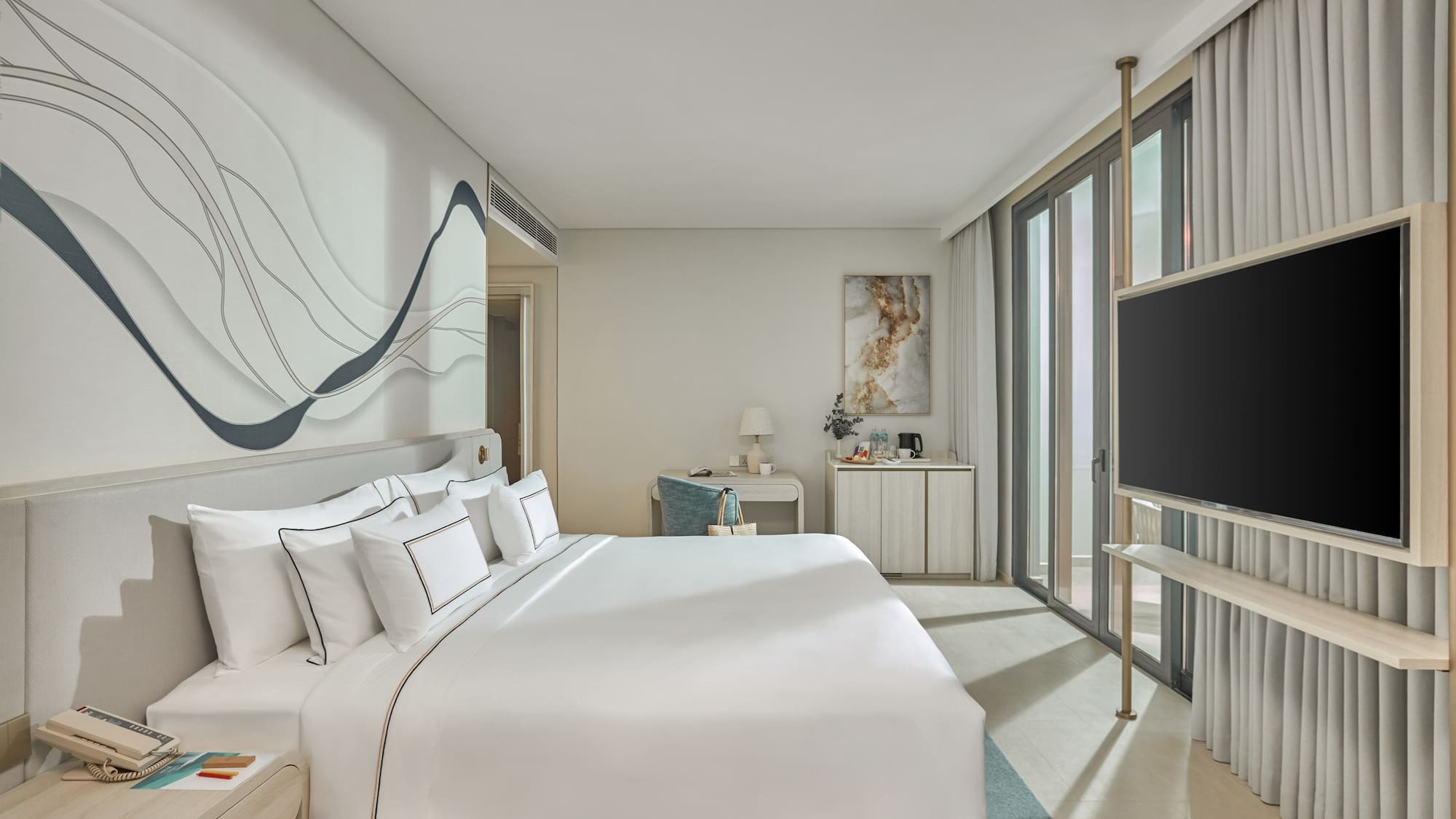 Modern hotel bedroom with white bed, abstract wall art, desk, and TV.