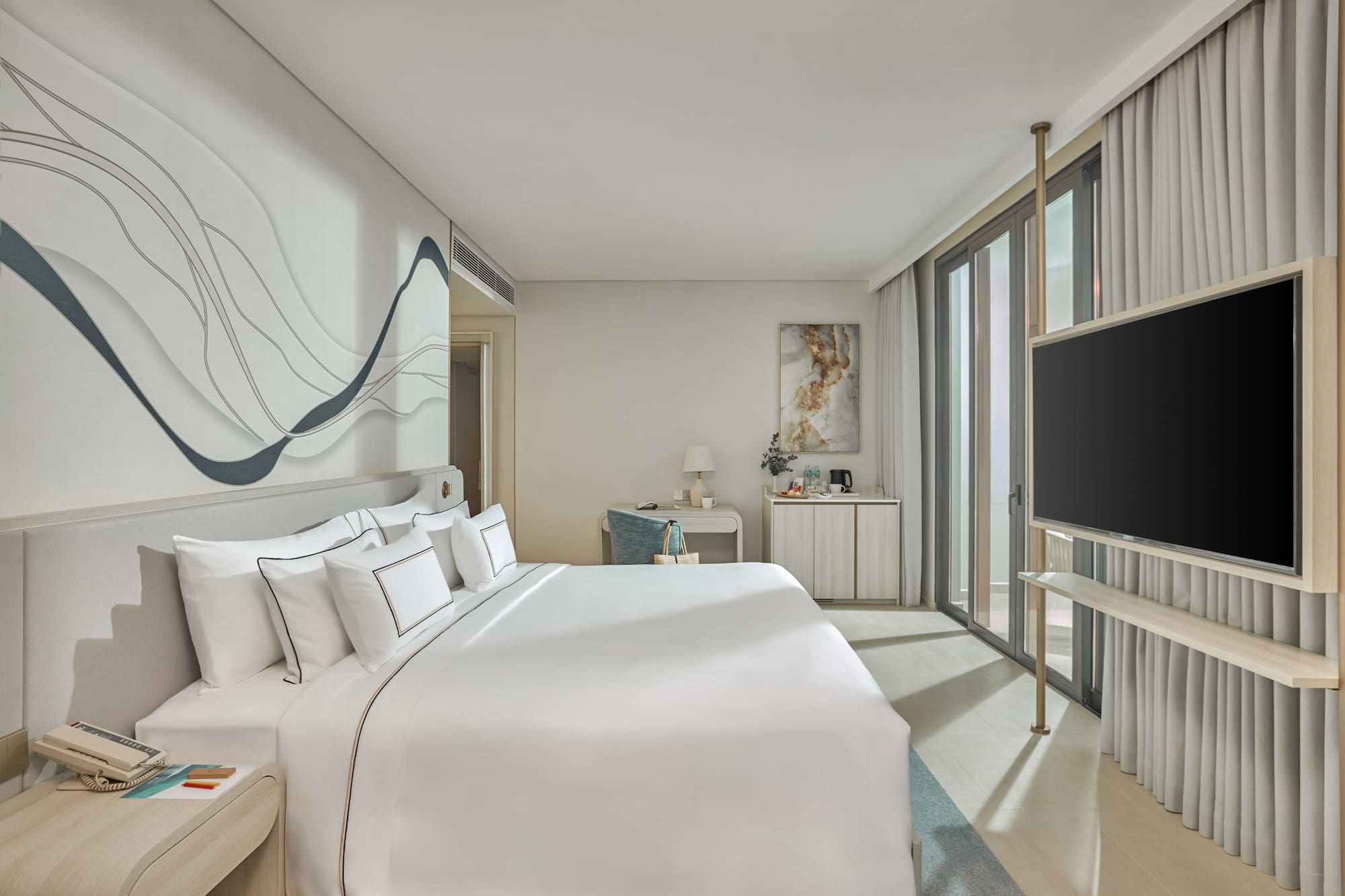 Modern hotel bedroom with white bed, abstract wall art, desk, and TV.