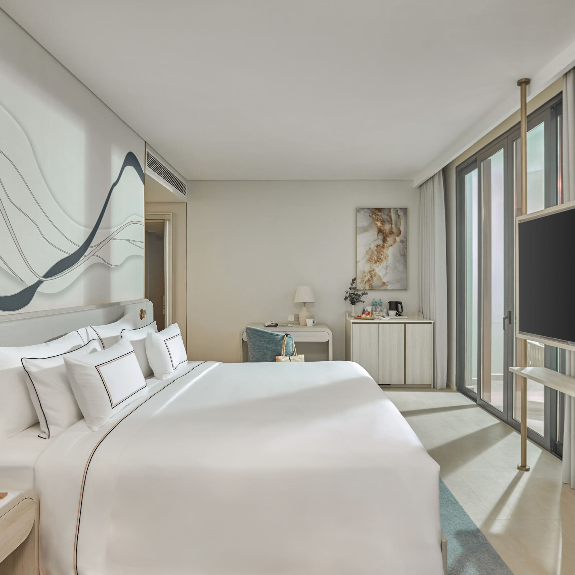 Modern hotel bedroom with white bed, abstract wall art, desk, and TV.