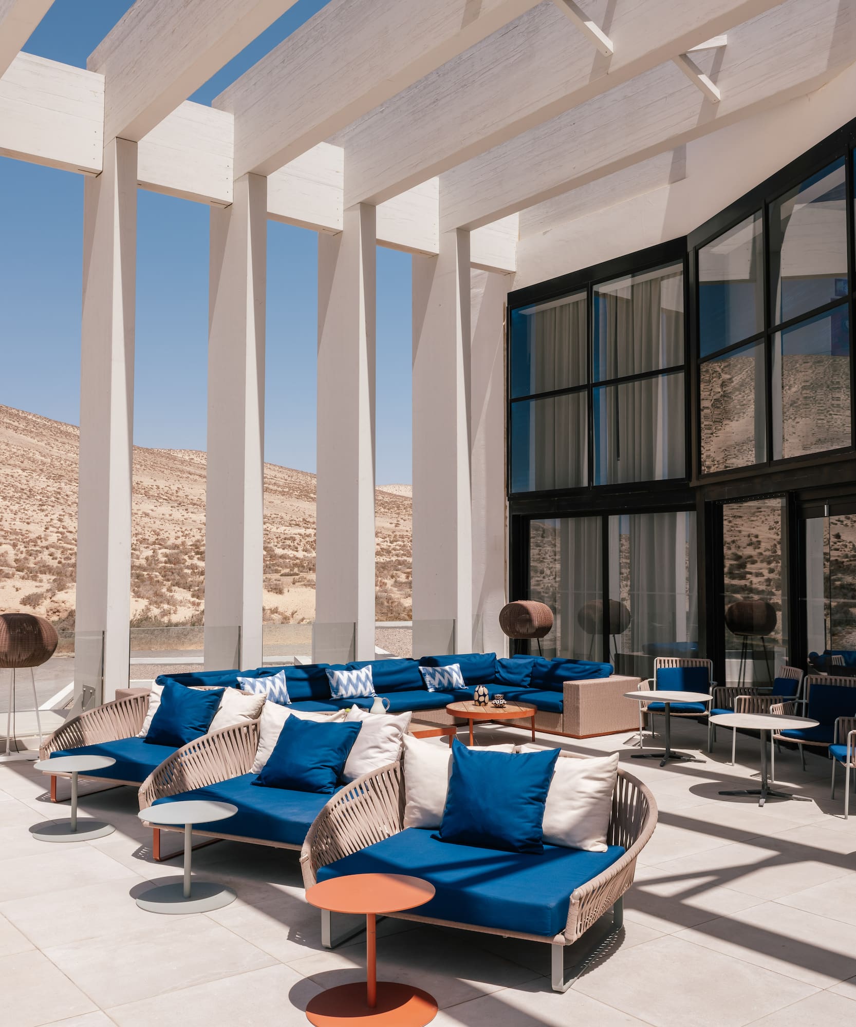 Modern desert resort lounge with blue sofas, mountain view, and white pergola.