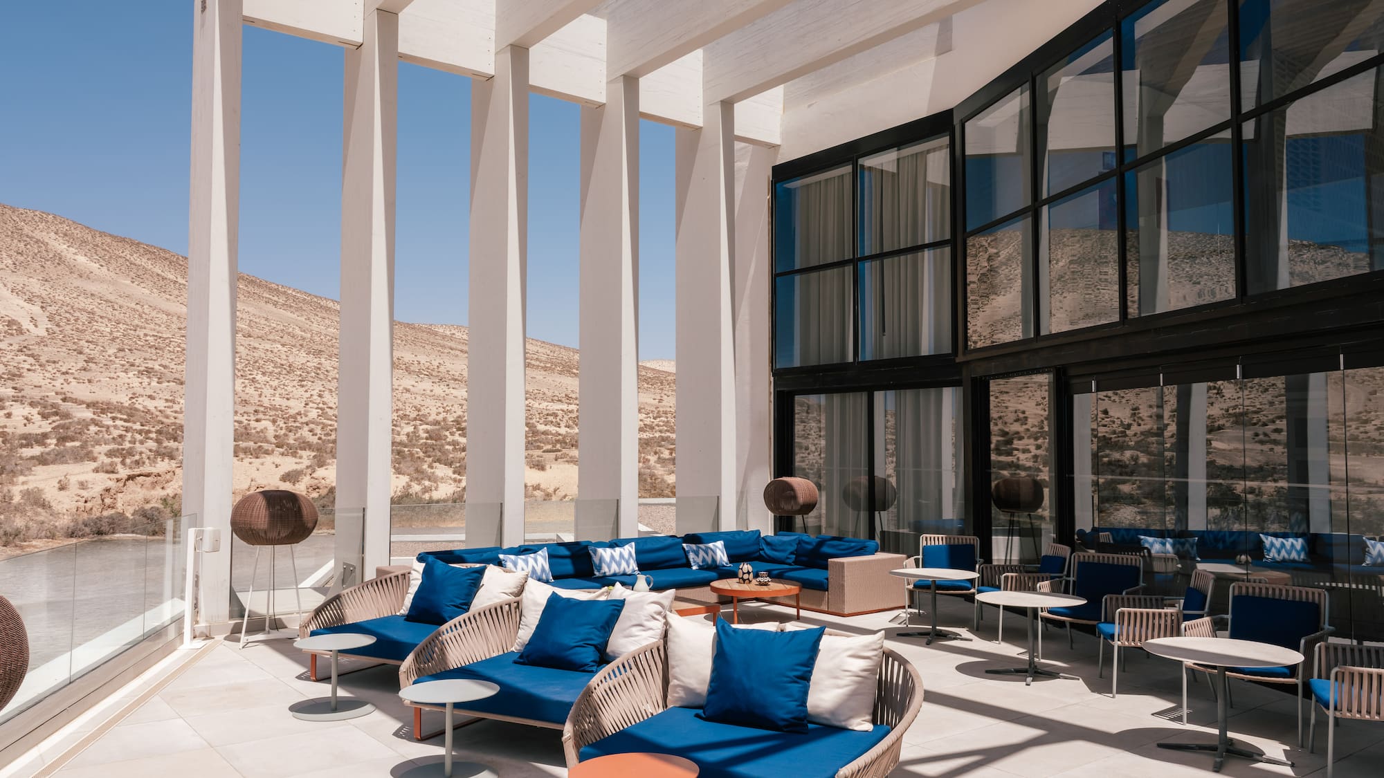 Modern outdoor lounge patio with blue furniture overlooking desert landscape and water.