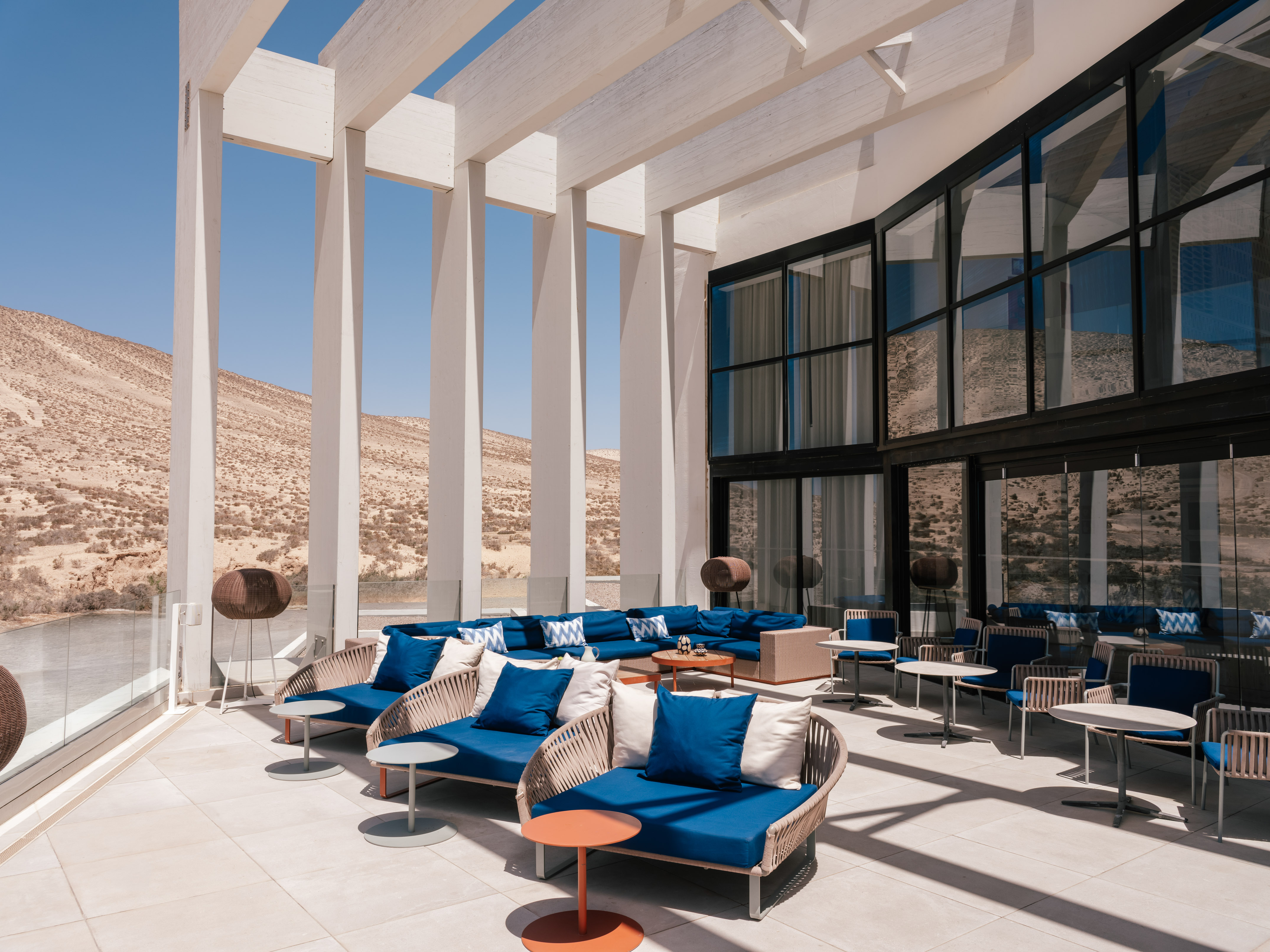 Modern desert resort lounge with blue sofas, mountain view, and white pergola.