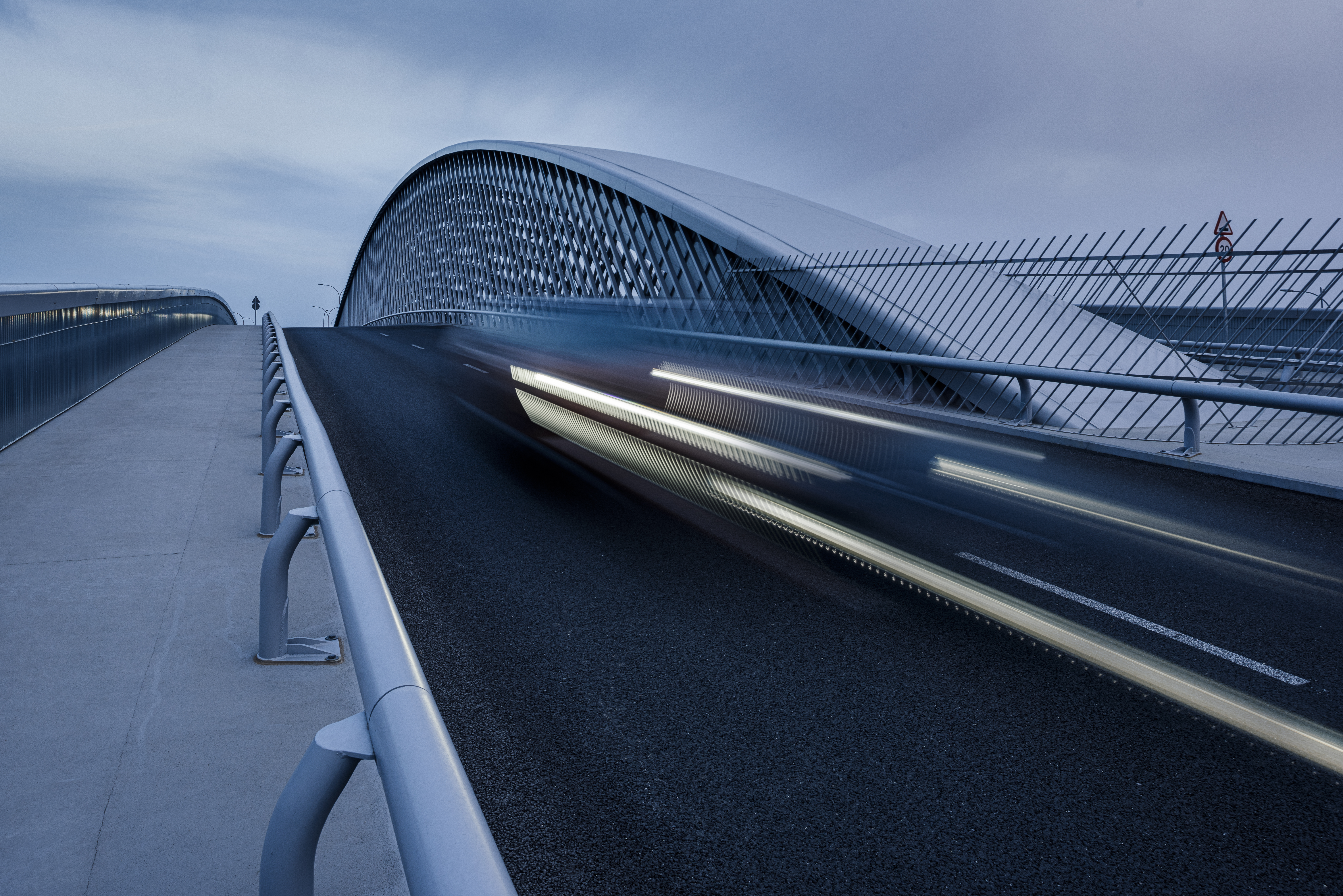 Motion blur light trails of a speeding car on a modern arched bridge at dusk.