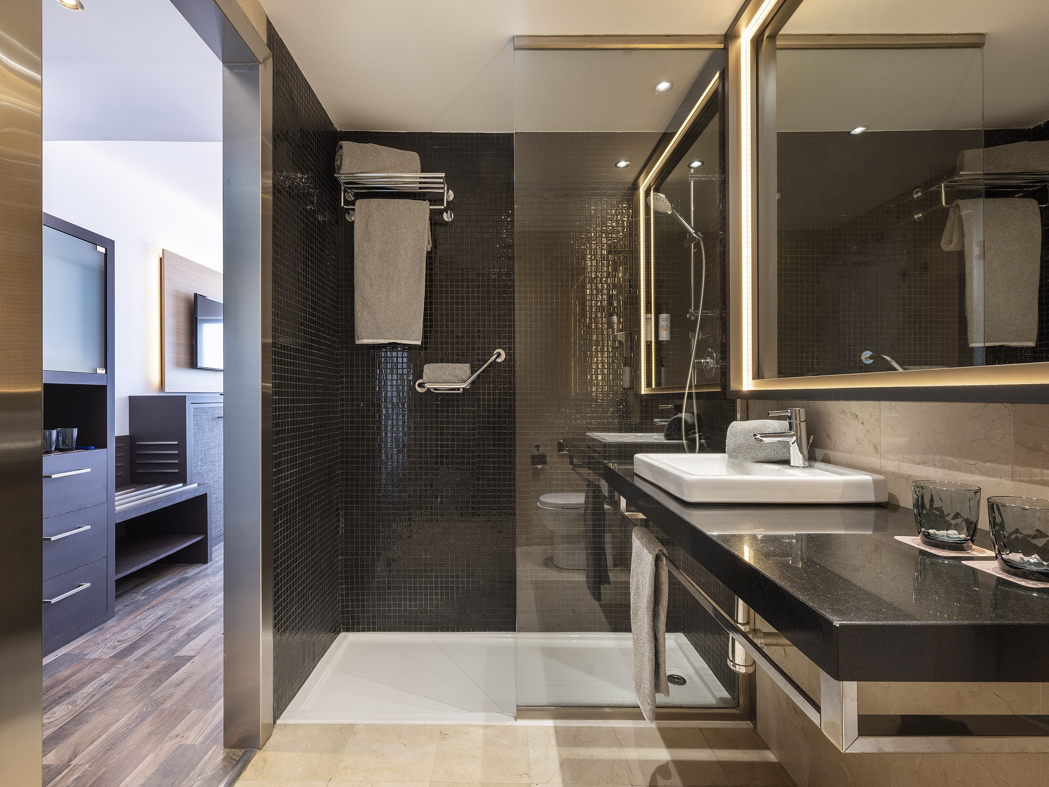 Modern bathroom with dark tiled glass shower, illuminated mirror, and vanity.