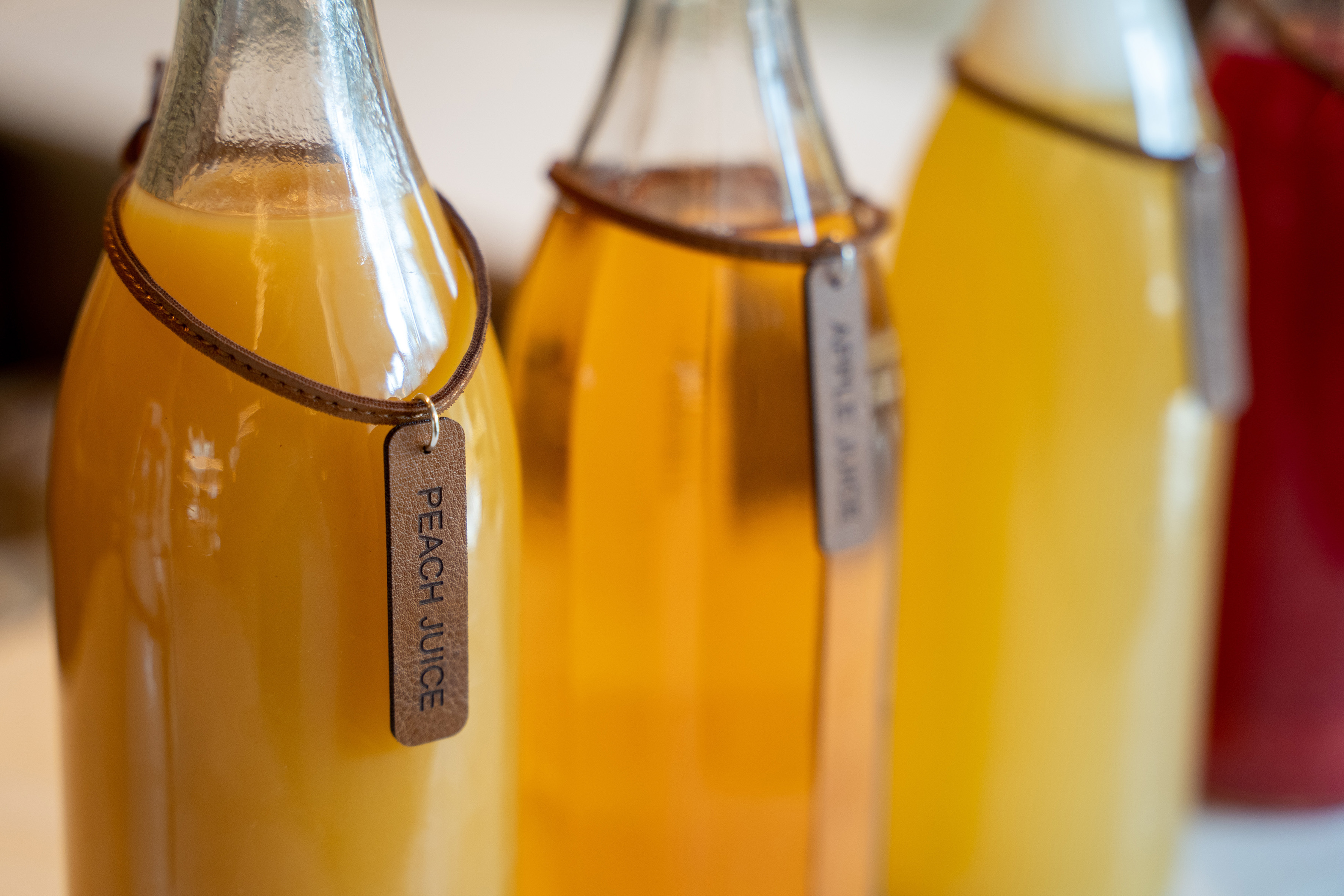 Peach and apple juice in labeled glass bottles, red juice background.