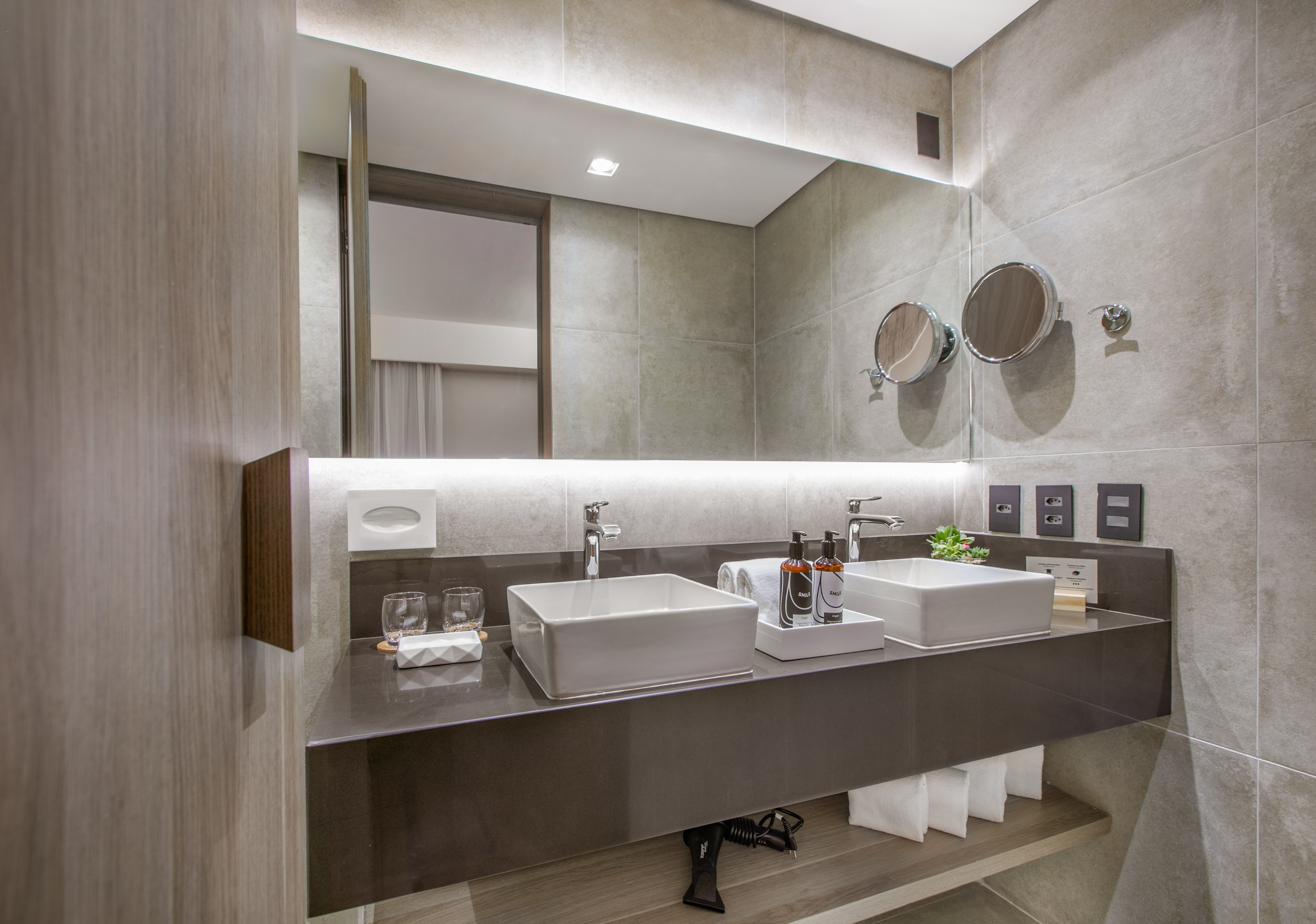 Modern hotel bathroom with double vanity, vessel sinks, and lighted mirror.