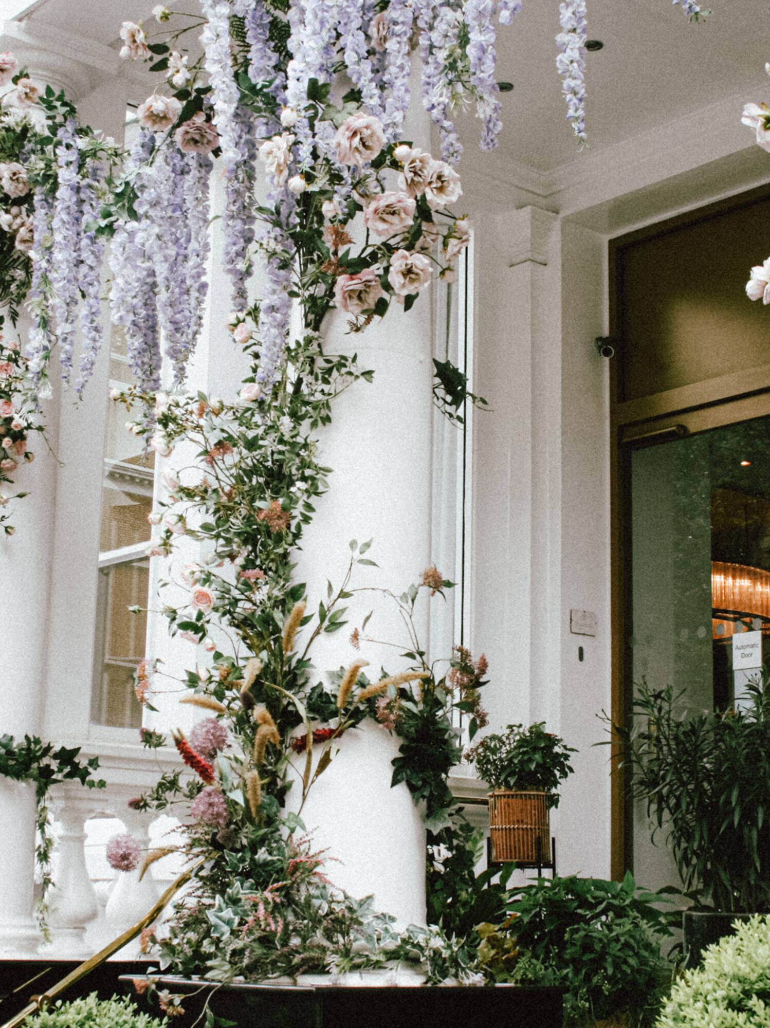 Entrada floral de edificio blanco con glicinas y rosas.