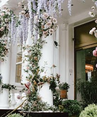 a white column with flowers and plants with Calleja de las Flores in the background