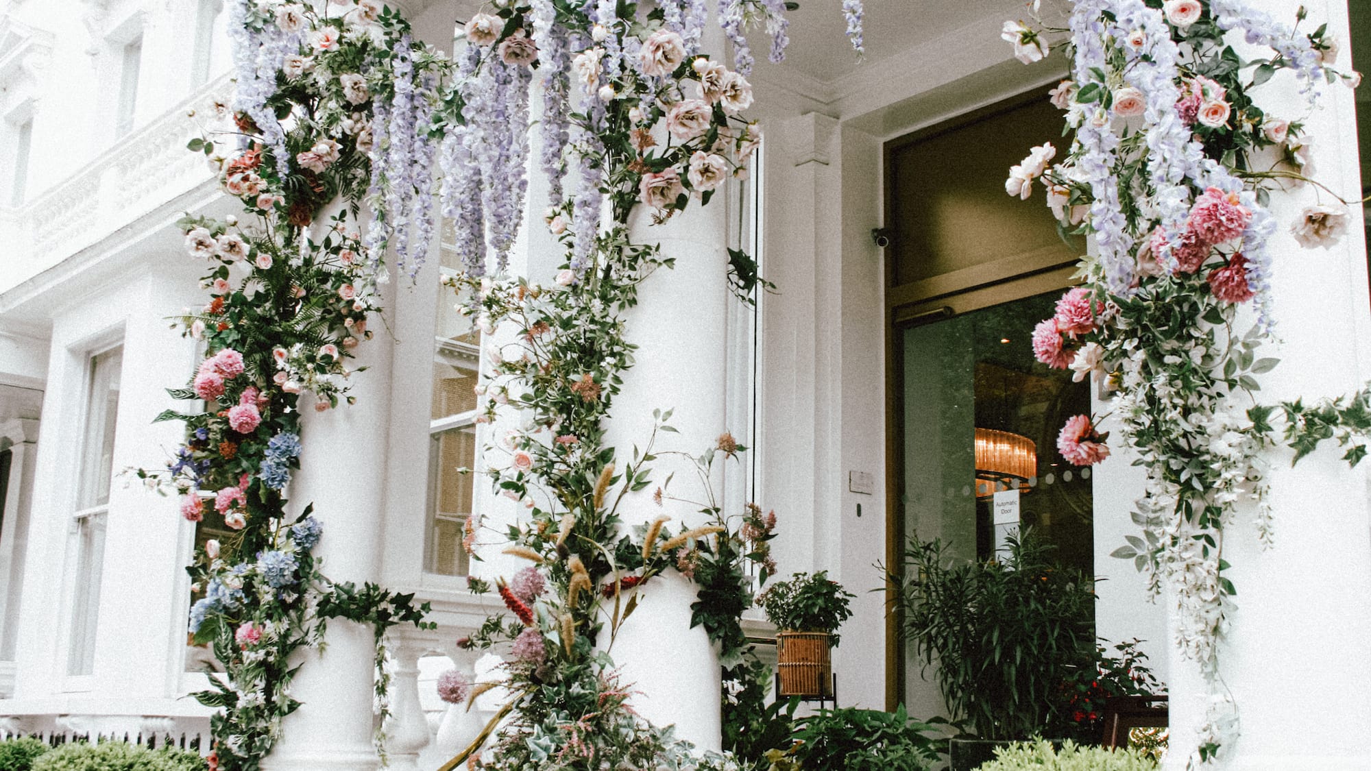 A white column adorned with flowers and plants stands against the backdrop of Calleja de las Flores.