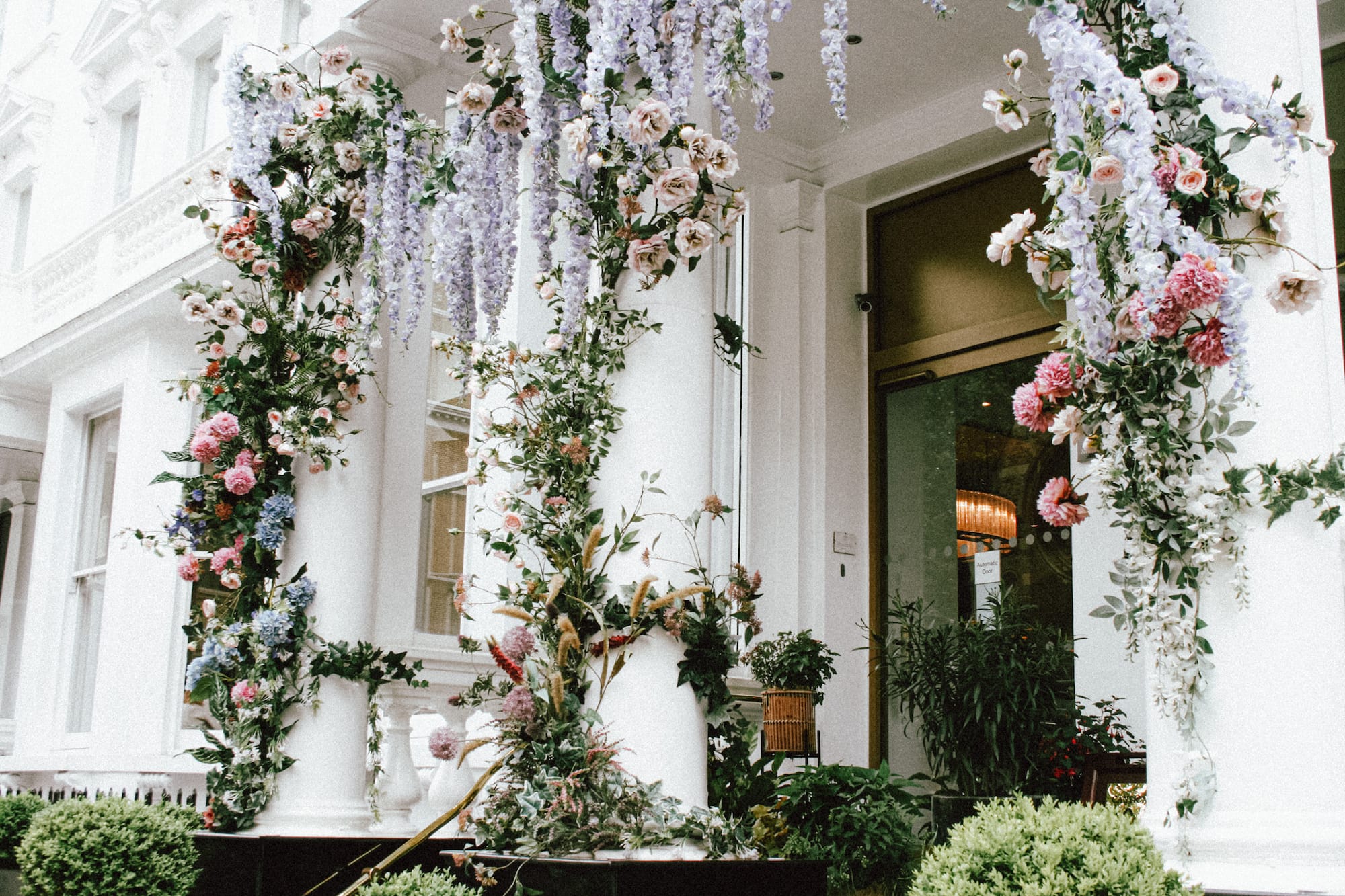 Entrada blanca con columnas, decoración floral, rosas, hortensias y glicinas.
