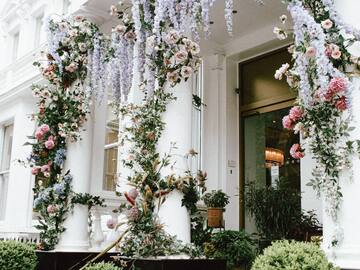 a white column with flowers and plants with Calleja de las Flores in the background