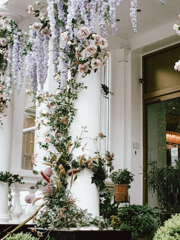 a white column with flowers and plants with Calleja de las Flores in the background