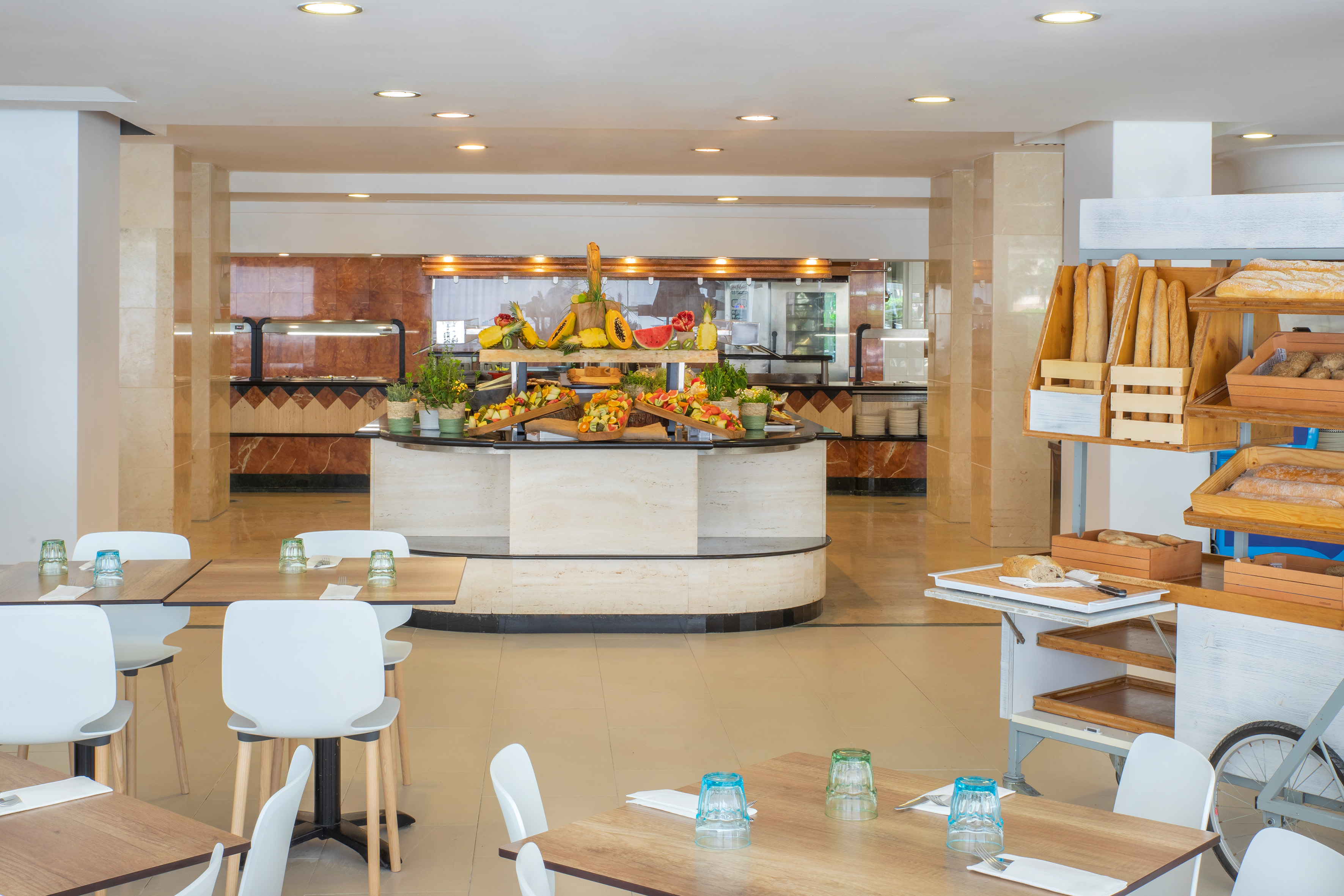 Resort buffet restaurant with fresh fruit and bread stations, set tables.