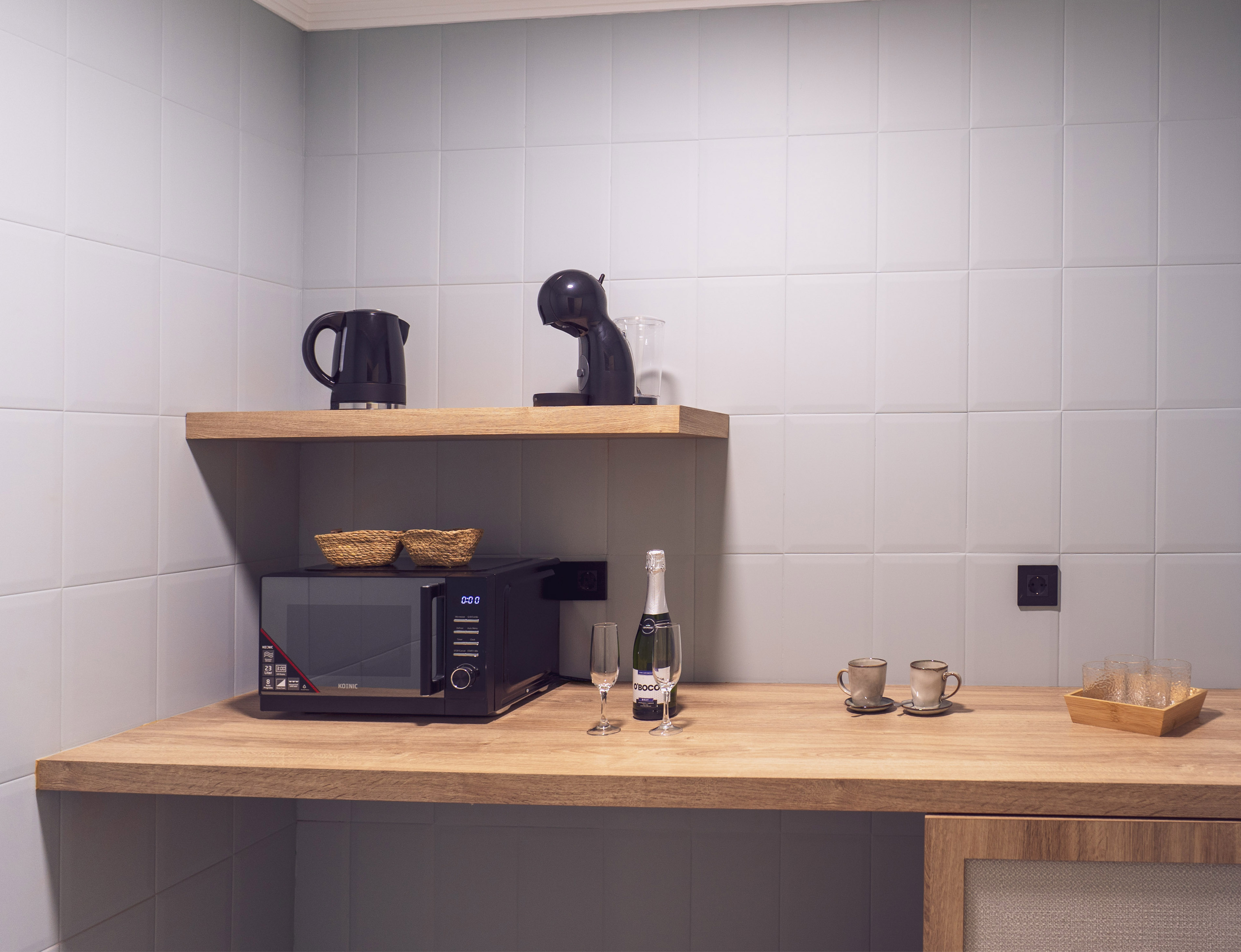 Compact kitchenette with microwave, coffee machine, kettle, and champagne.