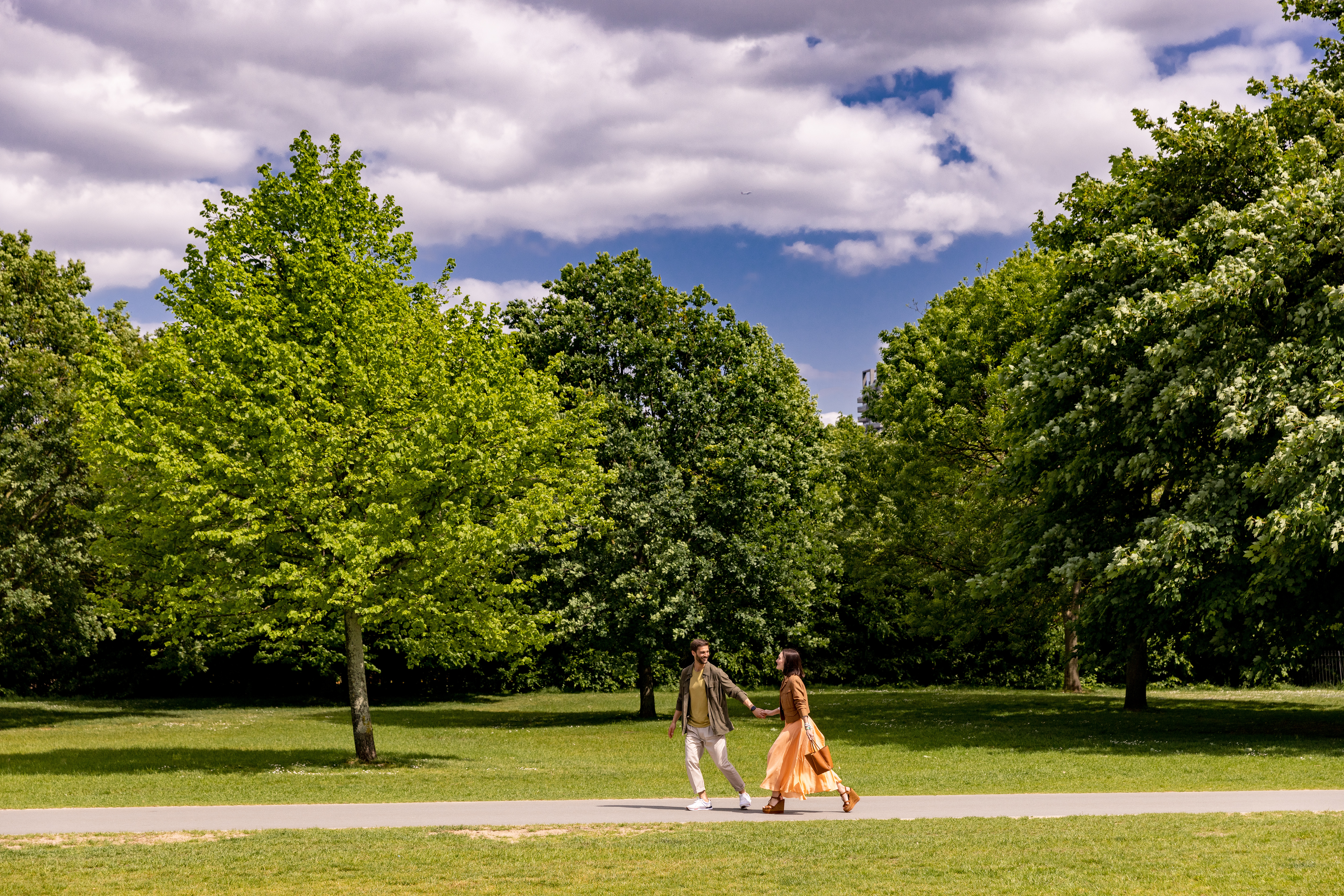 A man and a woman stroll through a park, hand in hand.