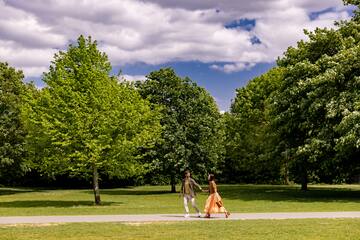 a man and woman holding hands and walking in a park