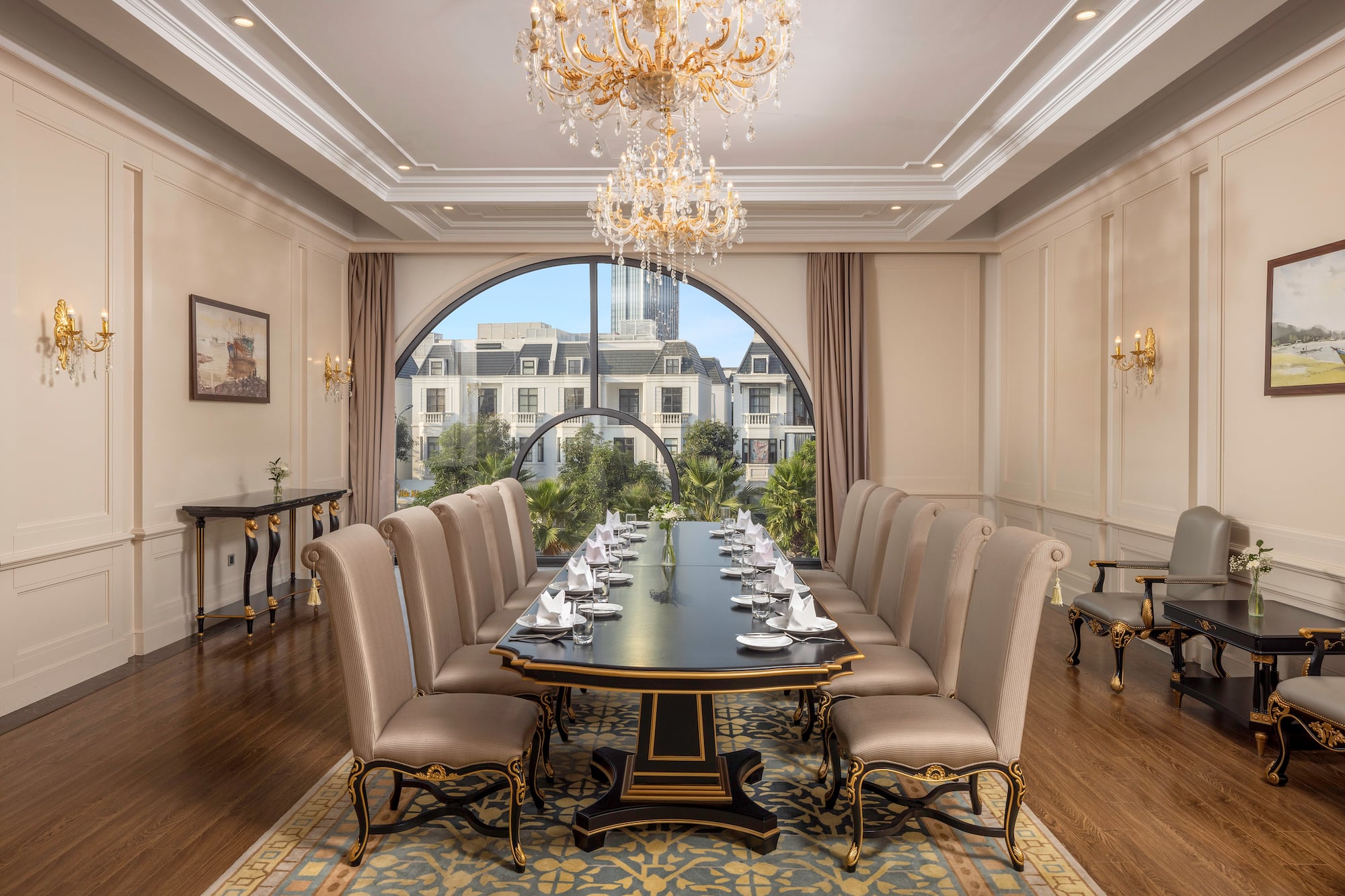 Elegant dining room with long table, chandeliers, and arched city view.