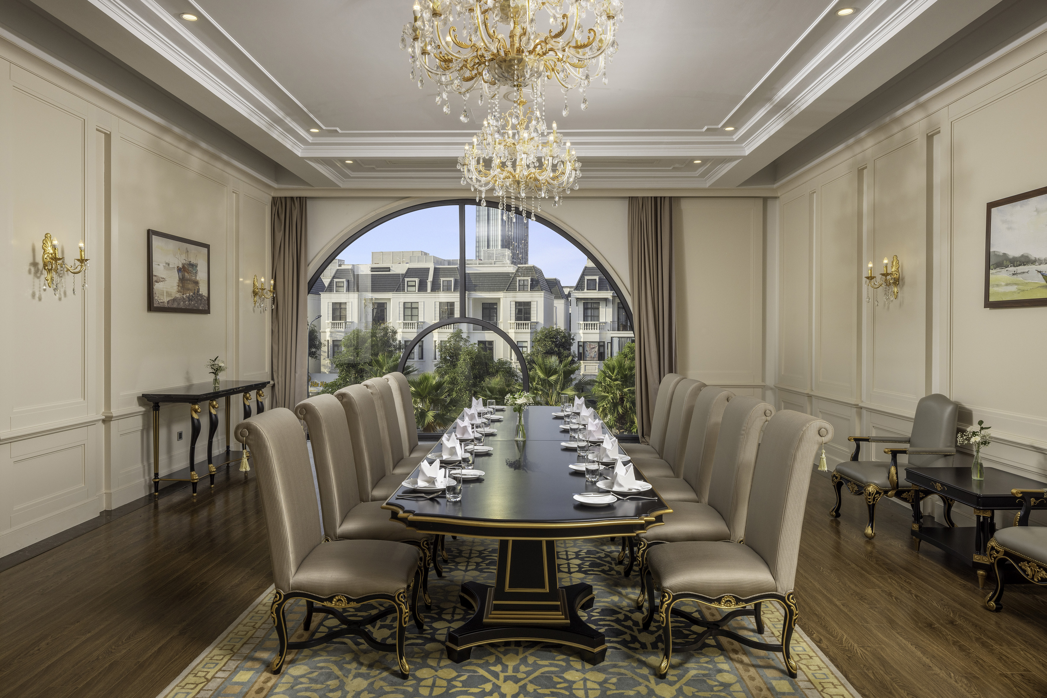 Elegant dining room with long table, chandeliers, and arched city view.
