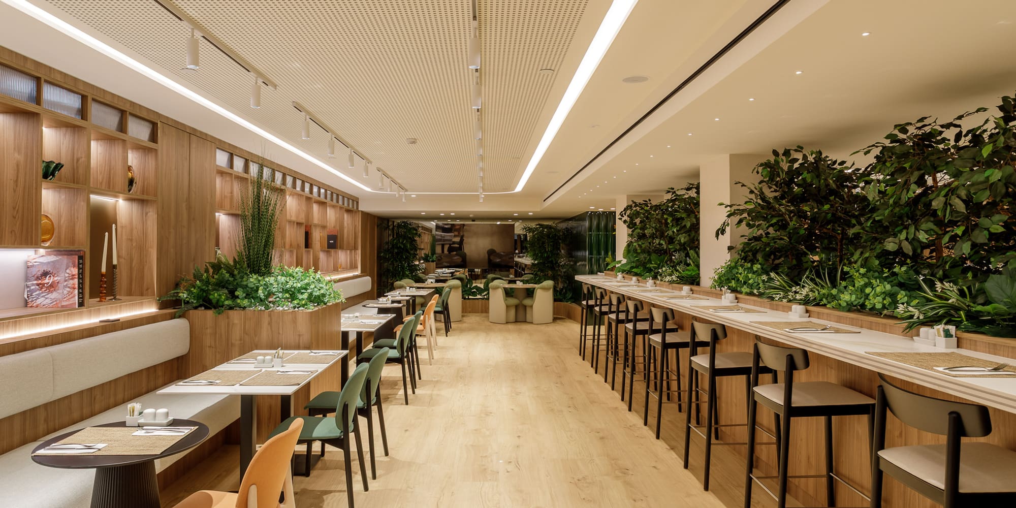 Modern dining area with natural wood, green plants, tables, and bar seating.