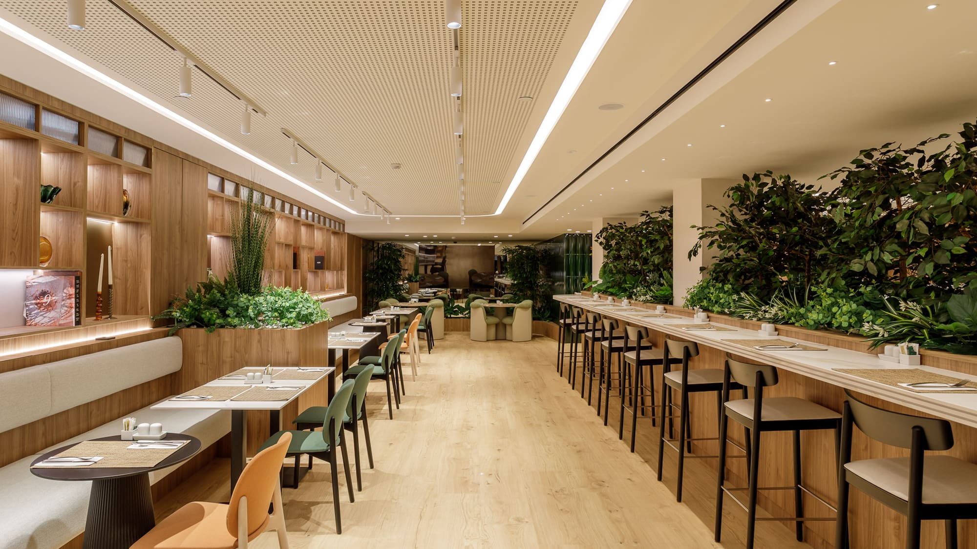 Modern dining area with natural wood, green plants, tables, and bar seating.