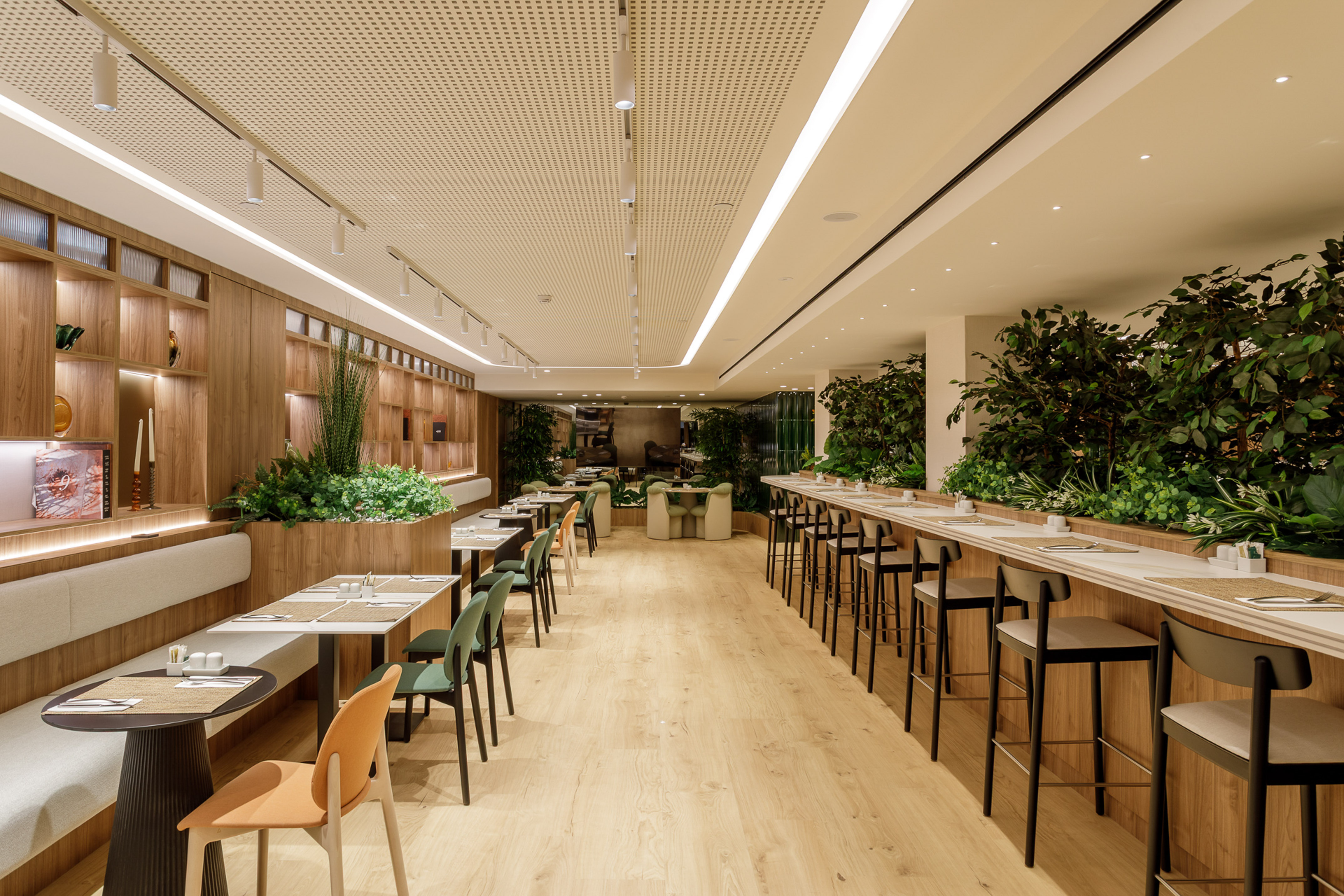 Modern dining area with natural wood, green plants, tables, and bar seating.