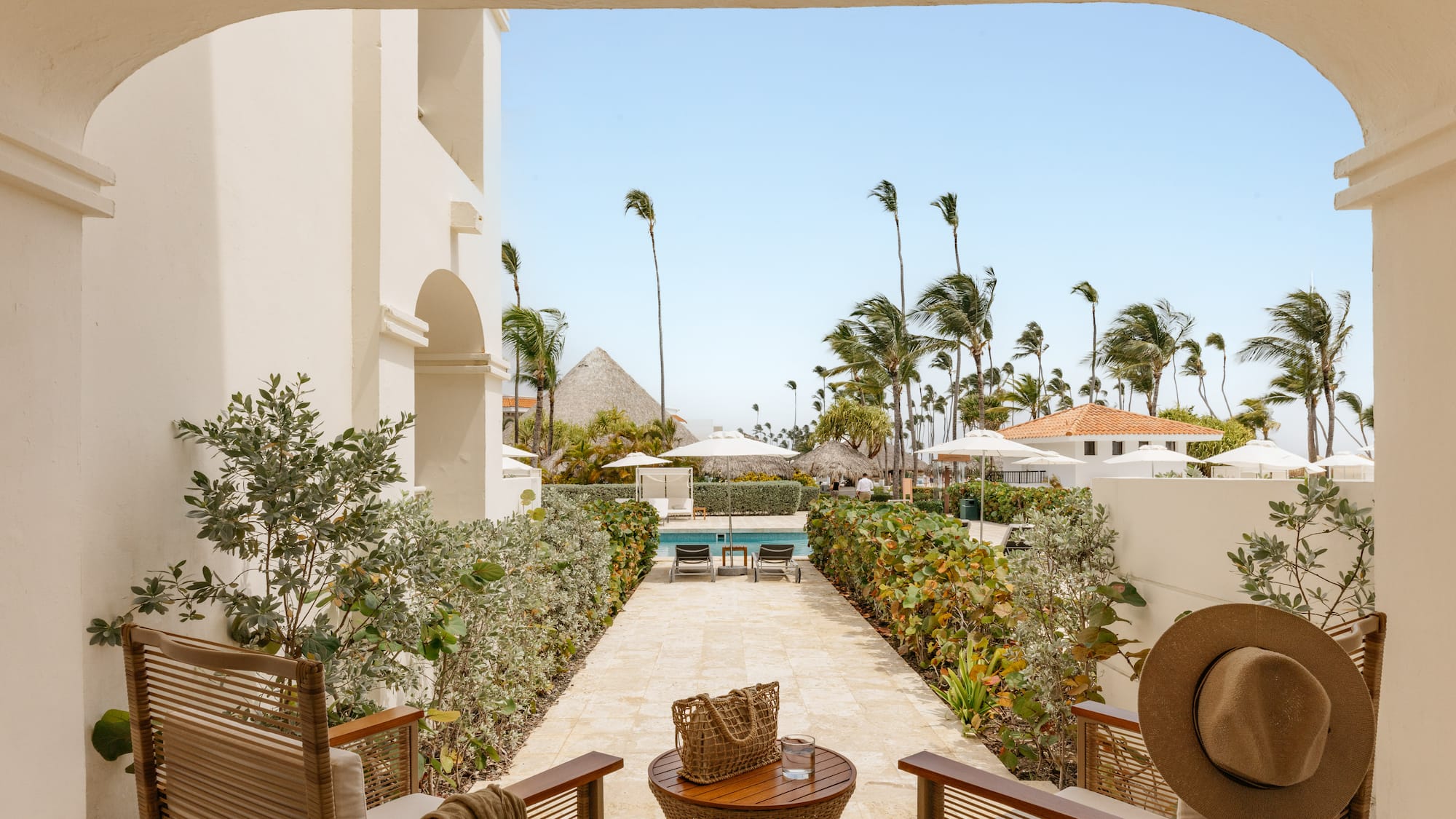Patio view of tropical resort pool, swaying palm trees, and sunny sky.