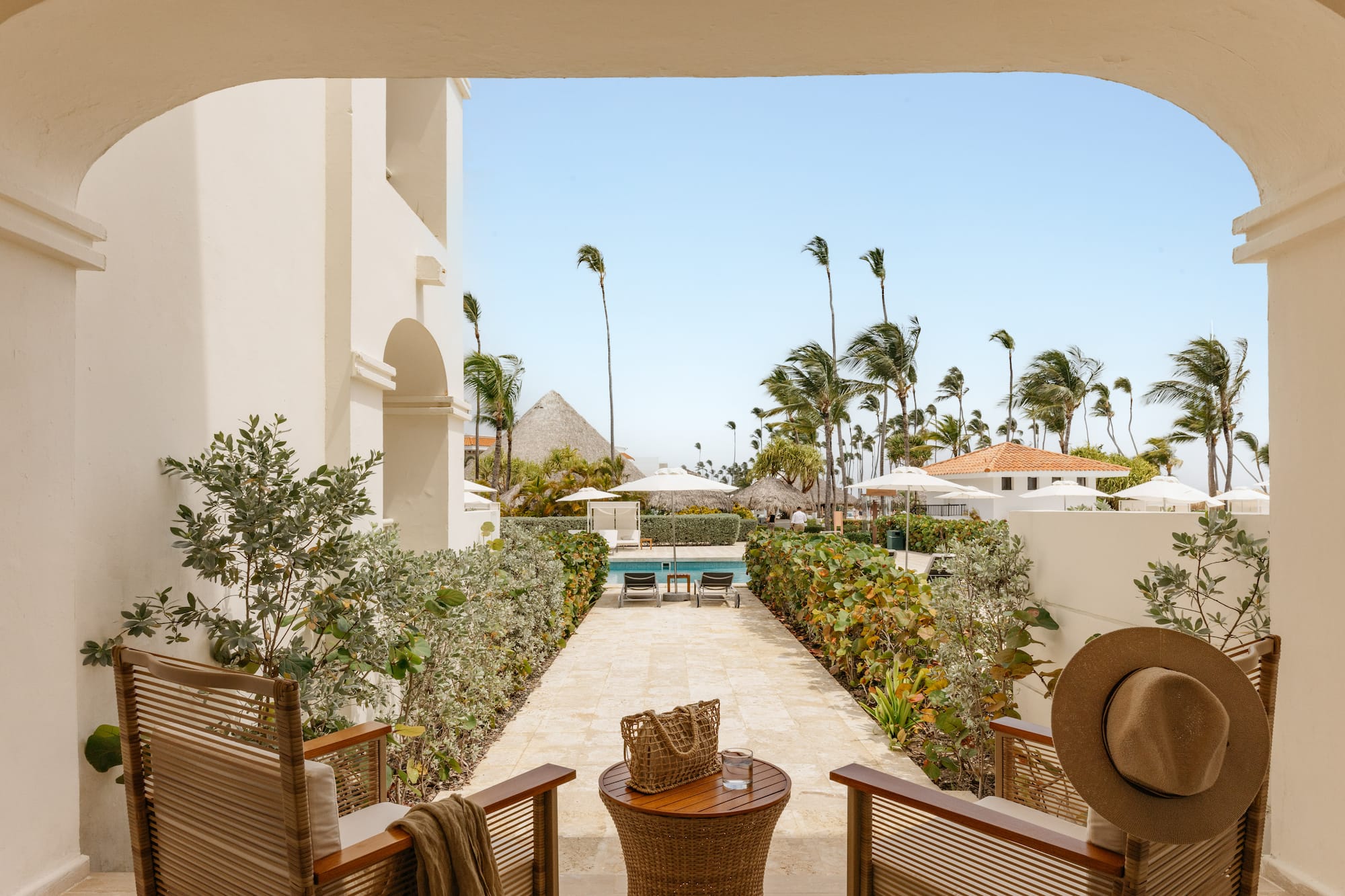 Patio view of tropical resort pool, swaying palm trees, and sunny sky.