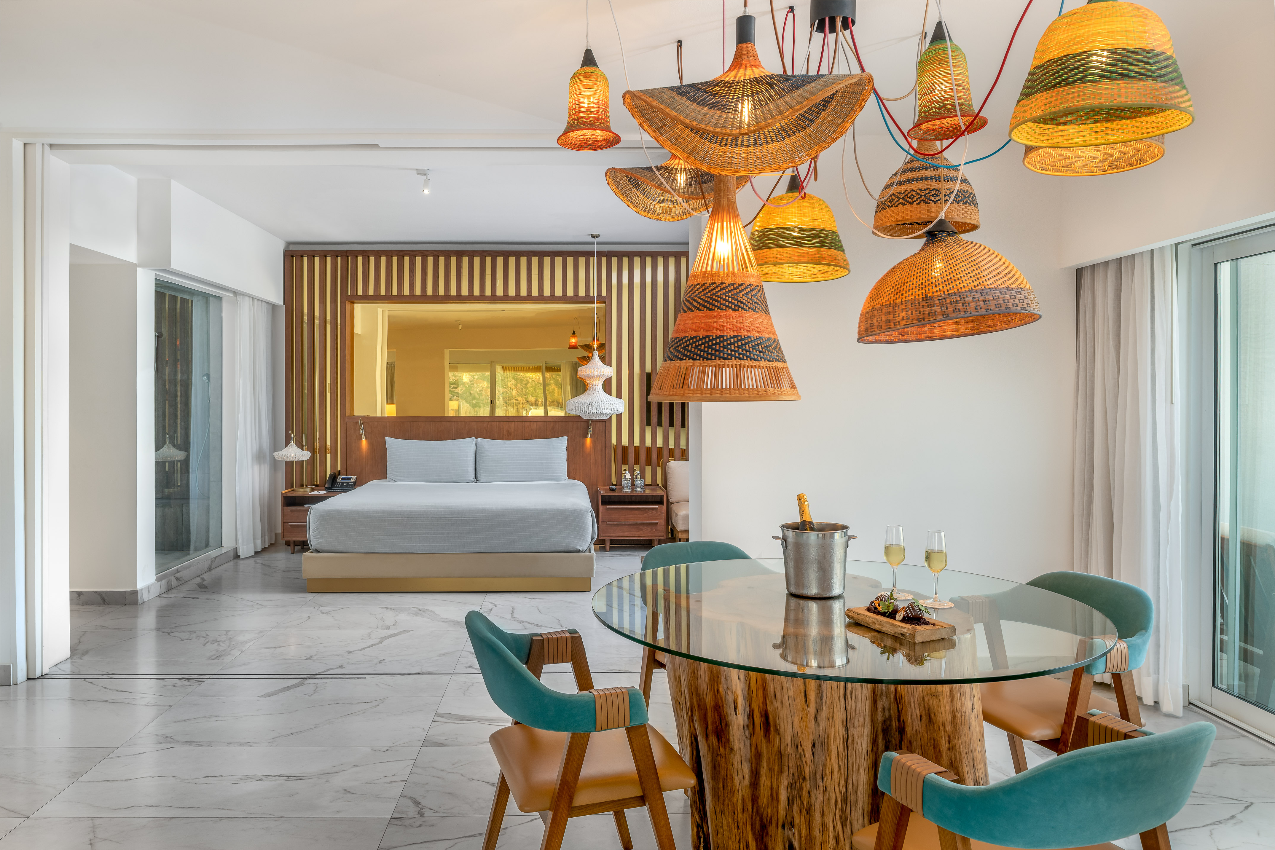 Modern hotel suite with bedroom, dining area, and unique woven pendant lights.